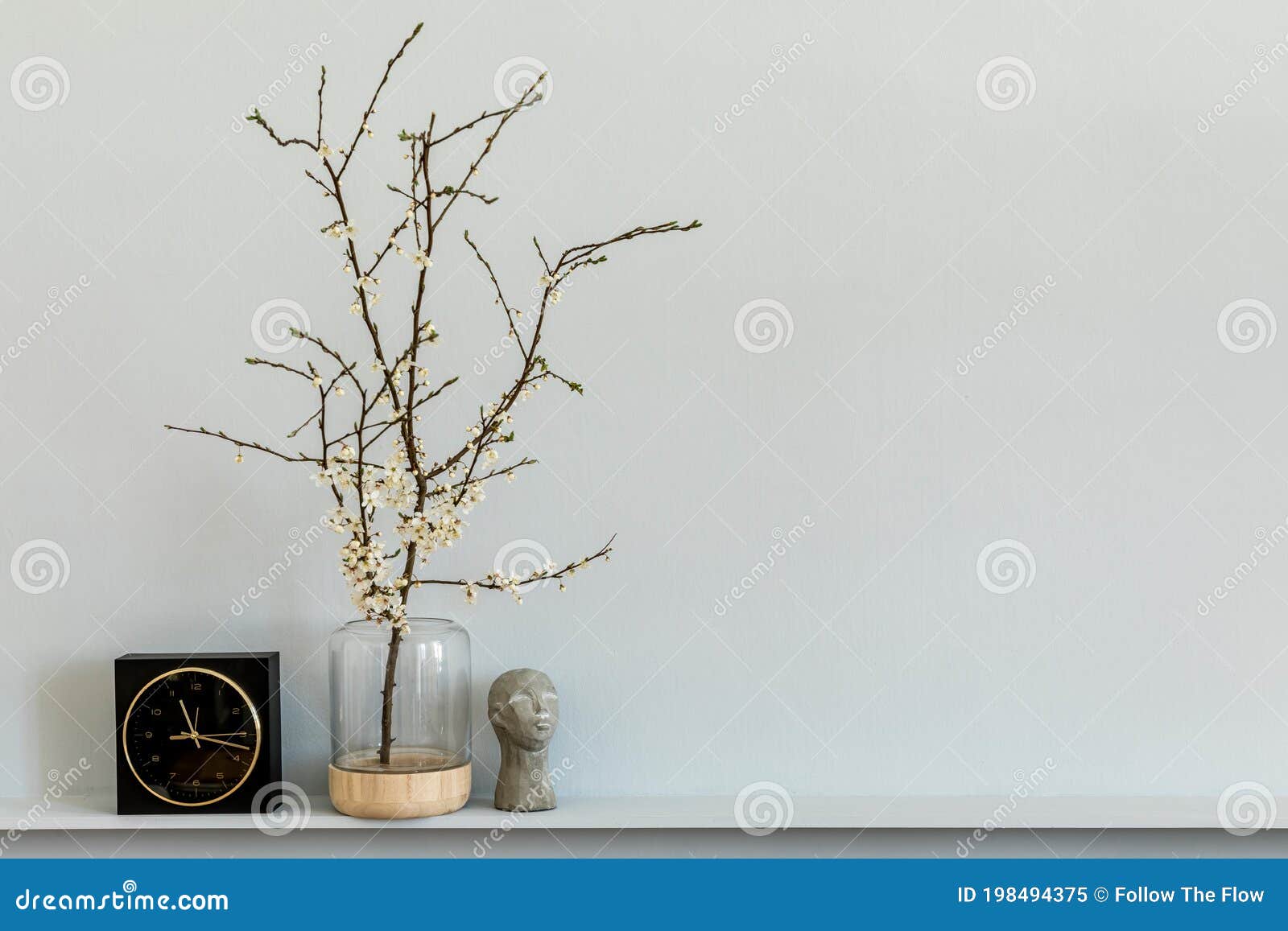 minimalistic composition on the shelf with dried flower in  vase, black clock and decoration. grey wall. copy space