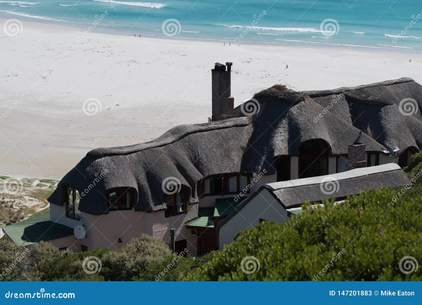 Mit Stroh gedecktes Häuschen, das einen Strand übersieht. Mit Stroh gedecktes Häuschen, das den Strand bei Noordhoek, Westkap übersieht