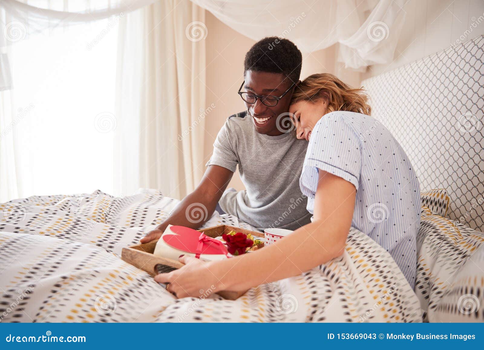 mixed race couple embracing, man bringing his partner breakfast and gifts in bed, close up