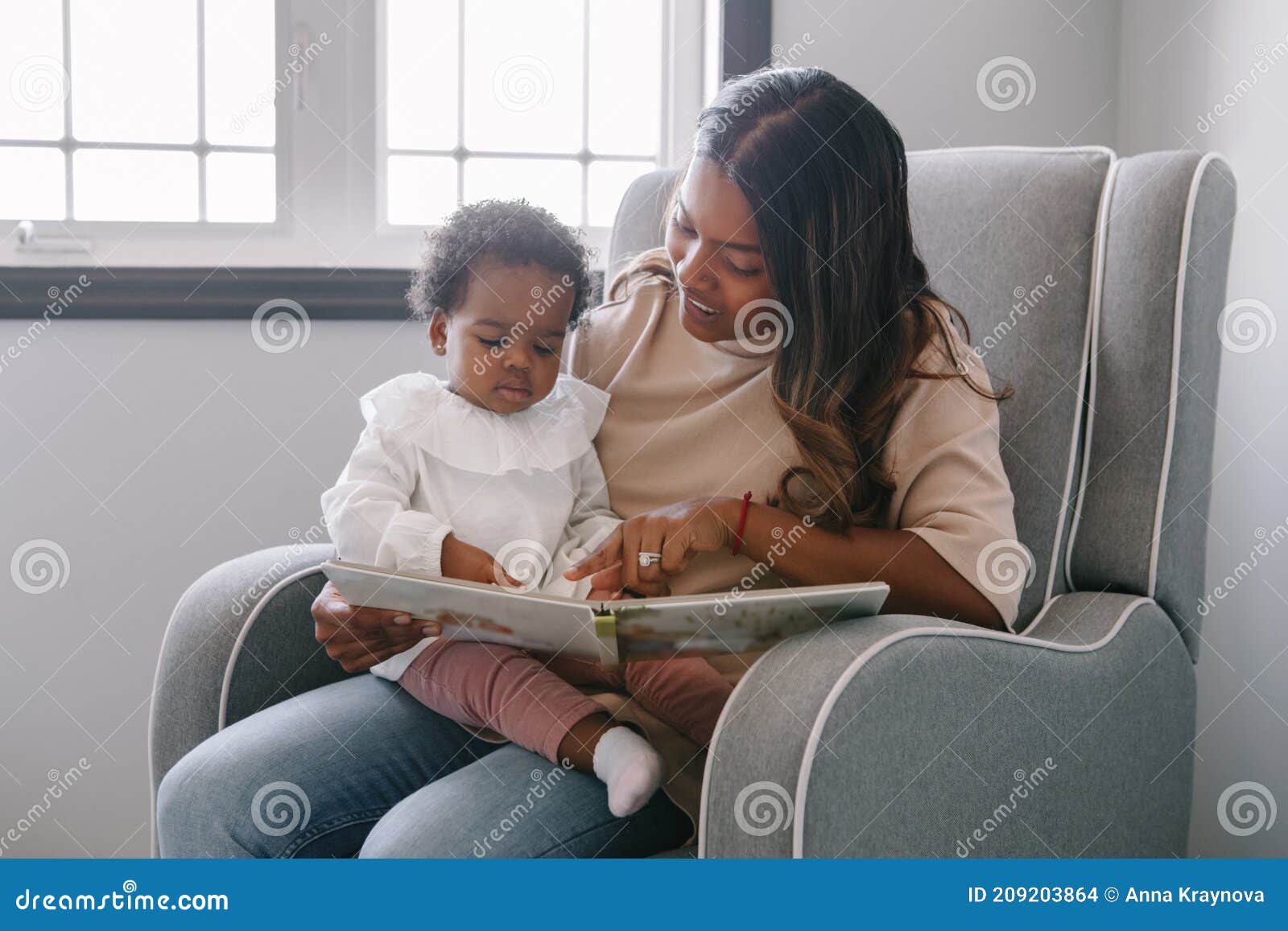 mixed race indian mom reading book with african black baby girl toddler at home. early age children education and development.