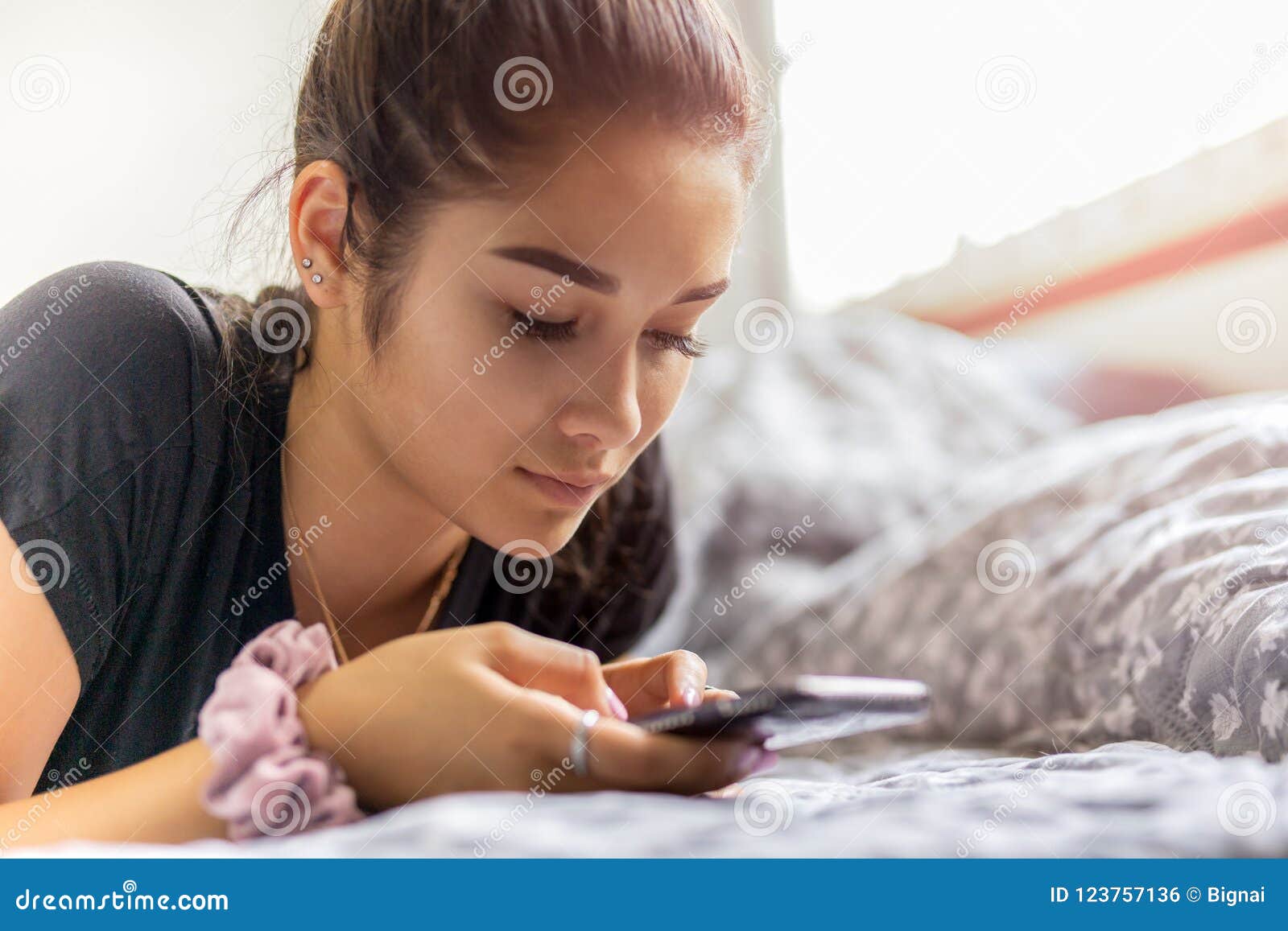 Mixed Race Teenage Woman Using Cell Phone While Laying In Bed Stock