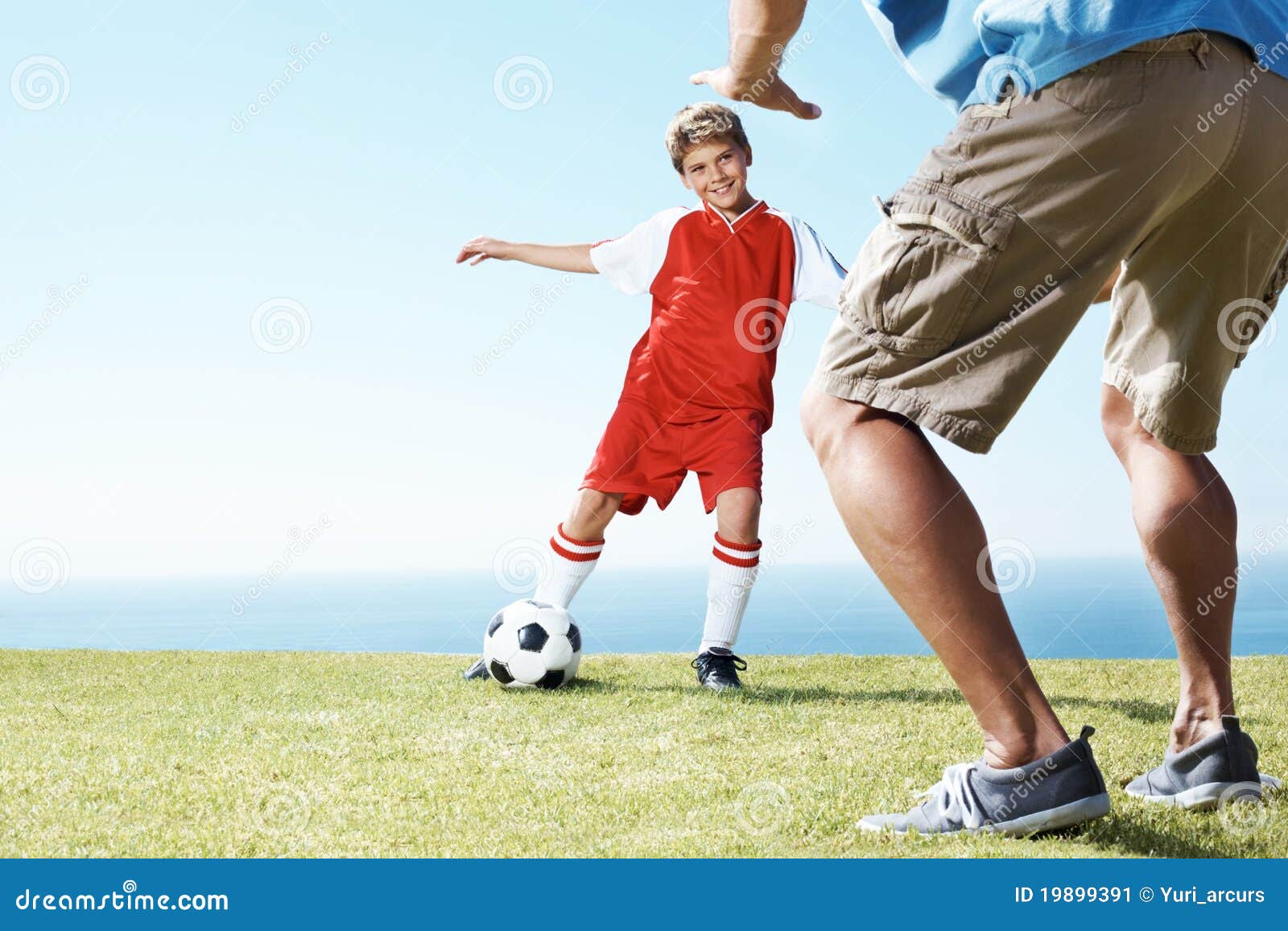 Miúdo pequeno que joga o futebol com seu pai no campo pelo mar