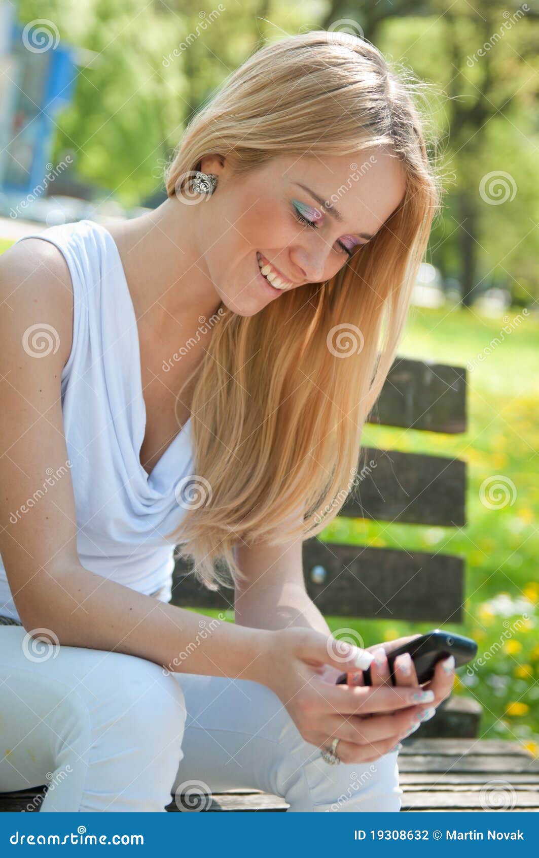 Mobiel communicatiemiddel - gelukkige tiener. Mobiel communicatiemiddel - glimlachende tiener die met smartphone in openlucht op zonnige dag werkt