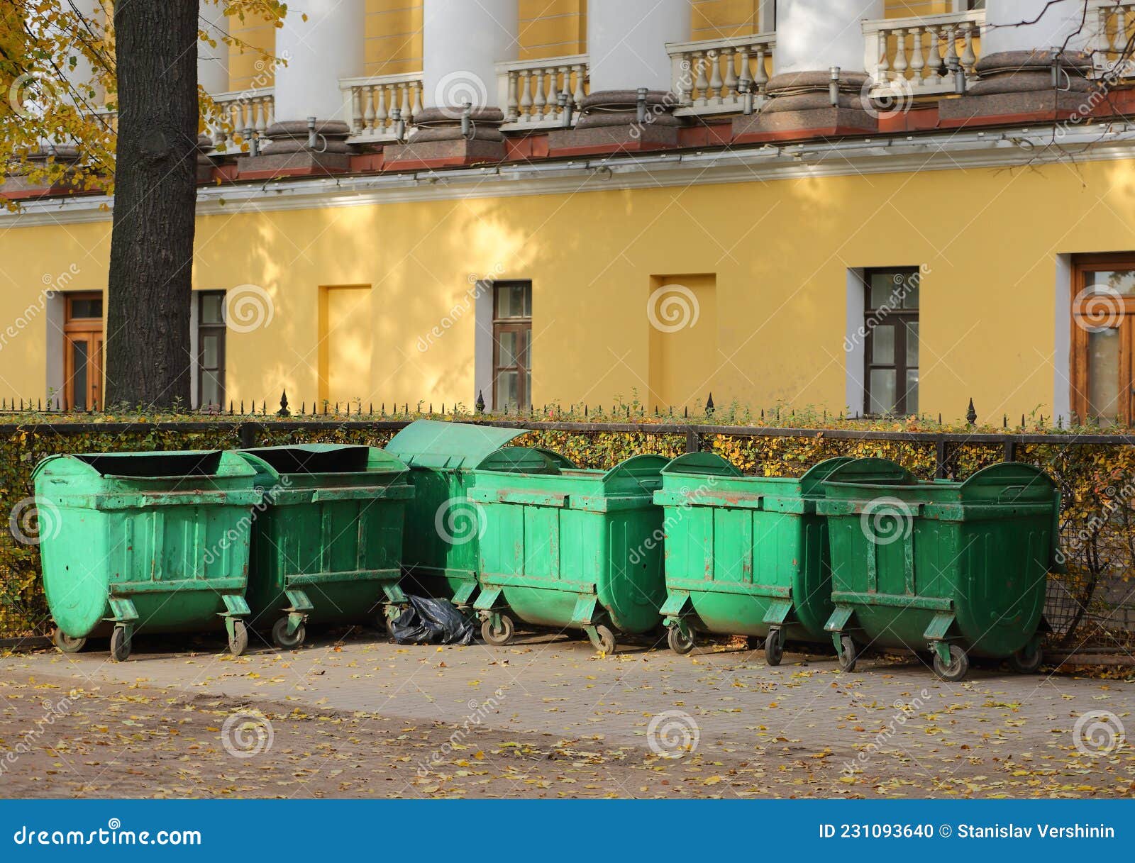 mobile plastic green garbage containers at the yellow wall of the old building