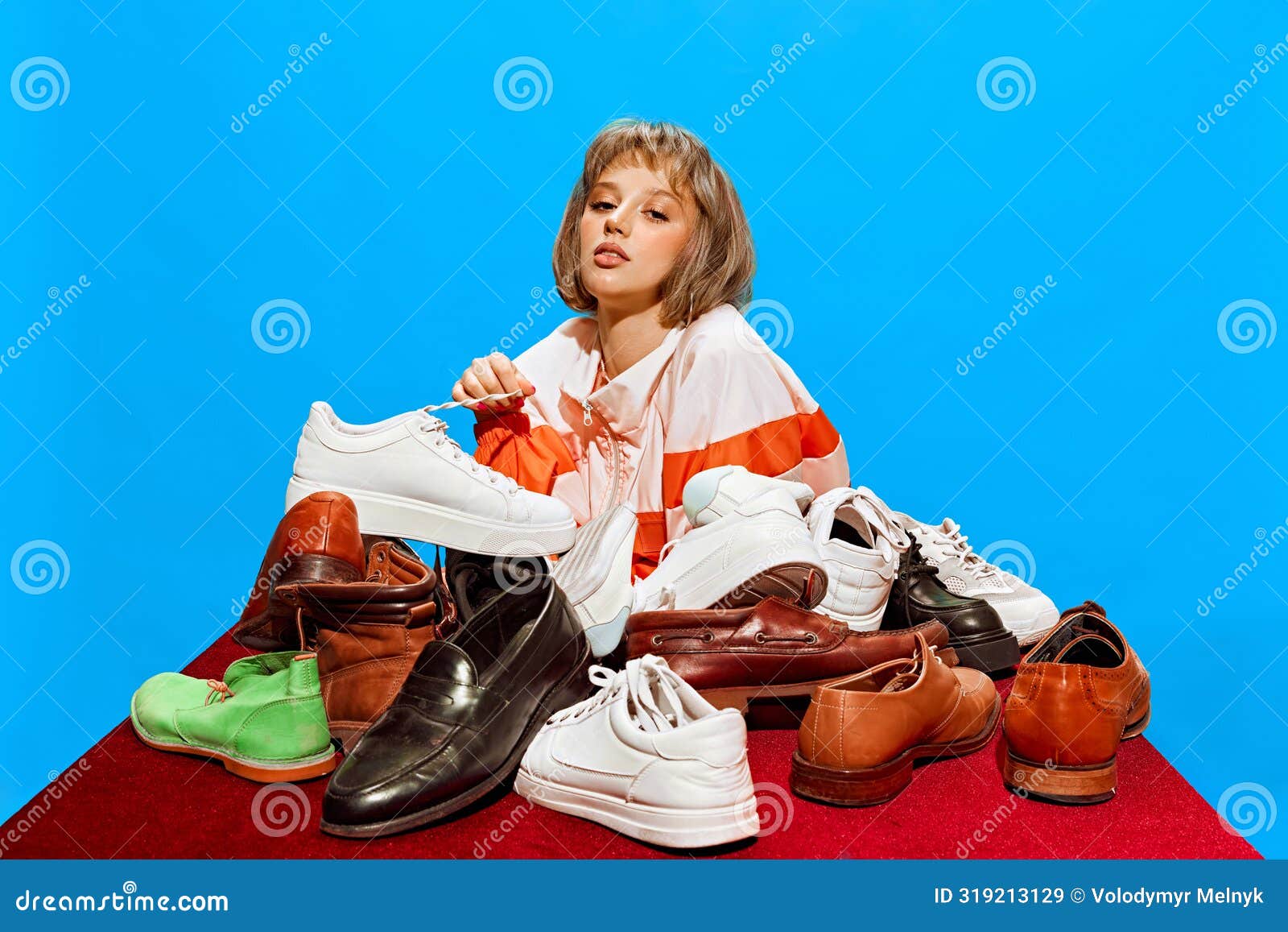 Mode Et Chaussures. Jeune Femme Chic Assise a Table Avec Diverses Chaussures Formant Pyramide Sur Fond Bleu. Chaussure Image stock Image du vente mode 319213129