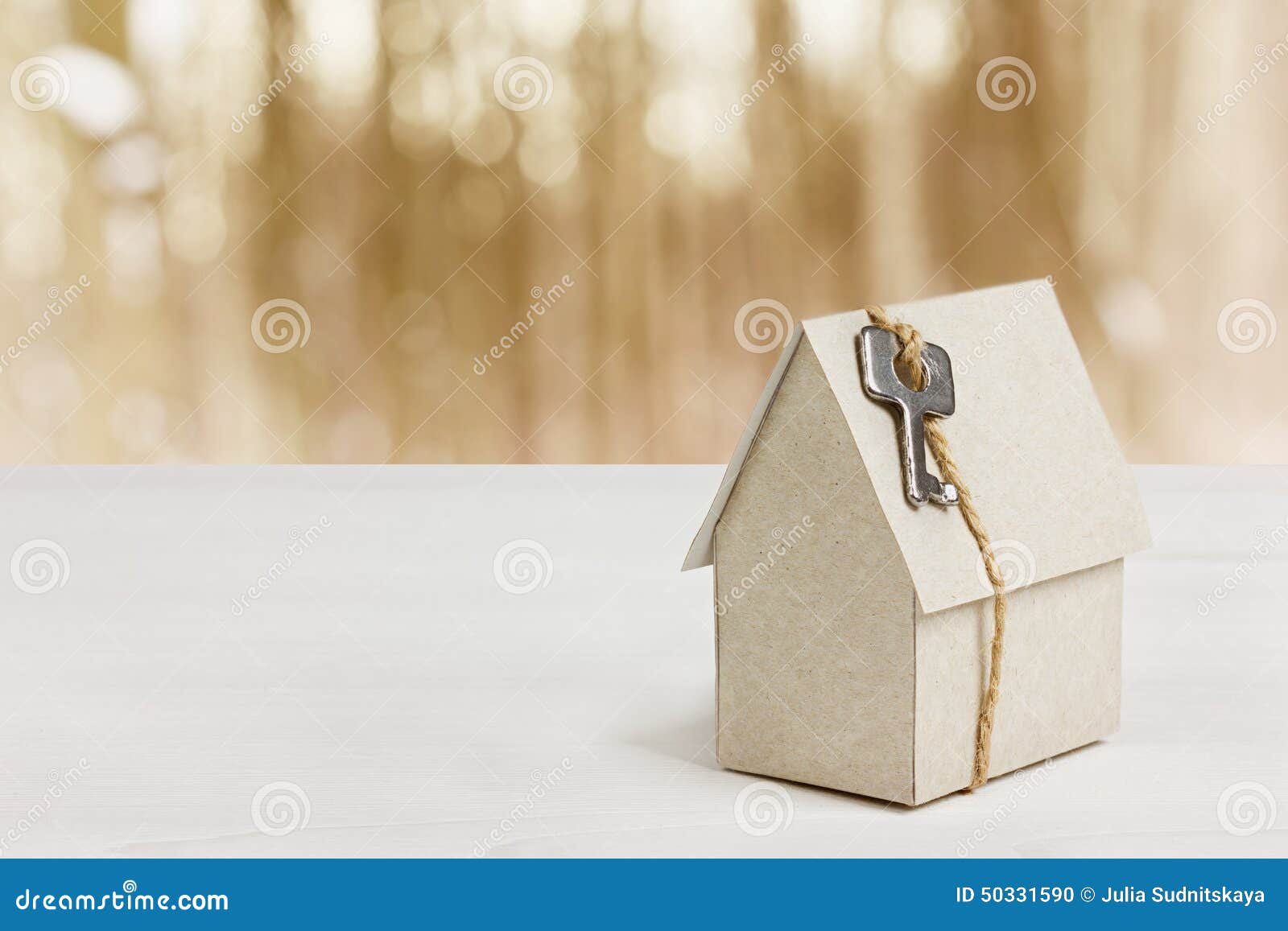 model of cardboard house with key against bokeh background. house building, loan, real estate or buying a new home