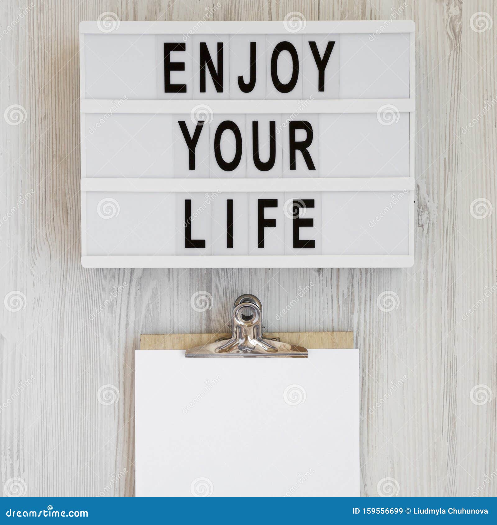 modern board with text `enjoy your life`, noticepad with blank sheet of paper on a white wooden background, top view. overhead,