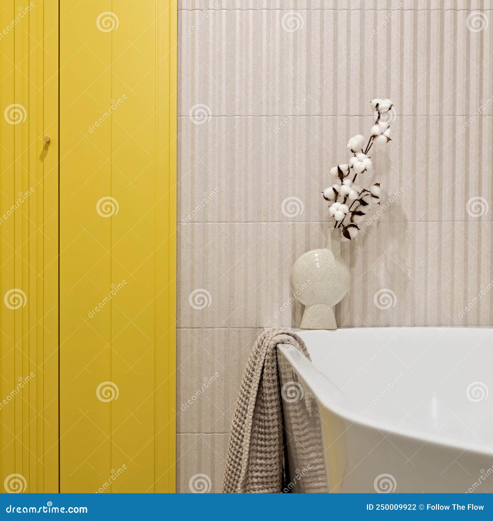 modern bright and yellow bathroom with lamella wall. big white bath with brown towel and dried flowers