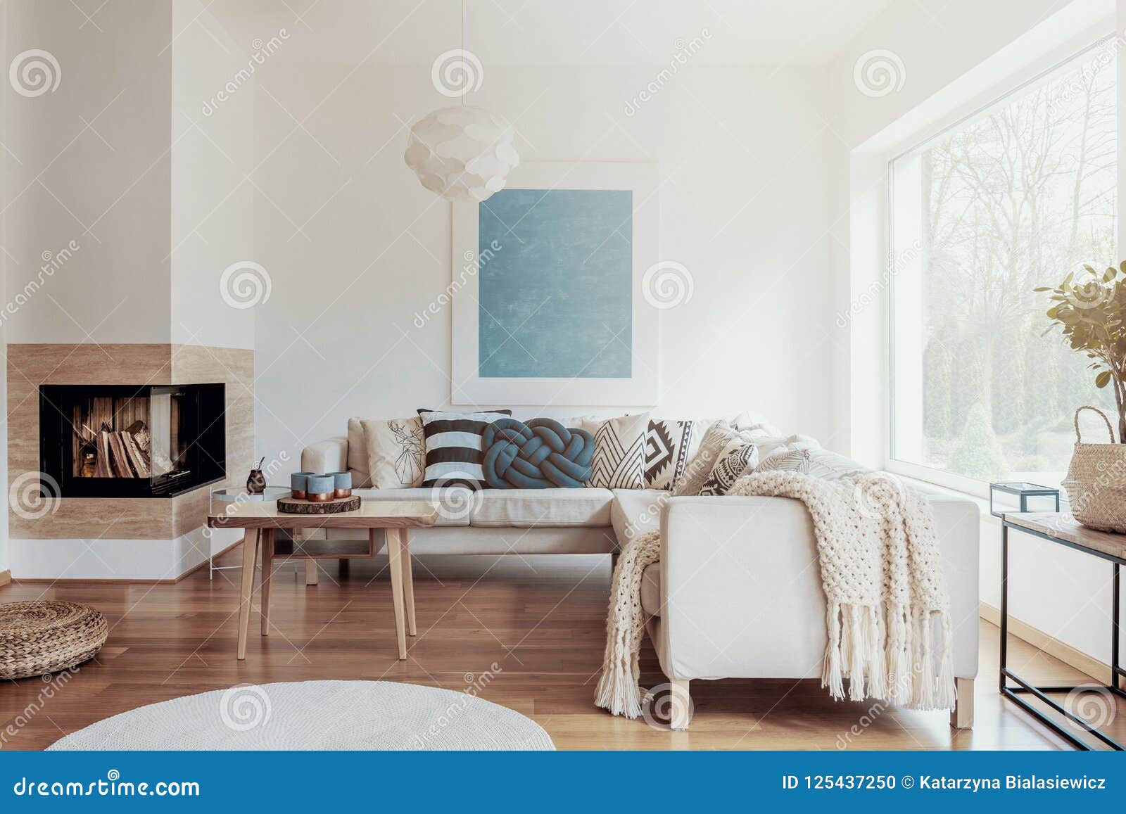 modern corner fireplace in a sunny, peaceful living room interior with white walls and cozy pillows and blankets on a beige sofa.