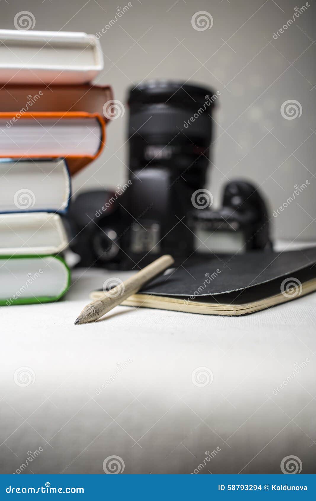 modern digital slr camera on the table next to a stack of books, and in the foreground a notebook and pencil.