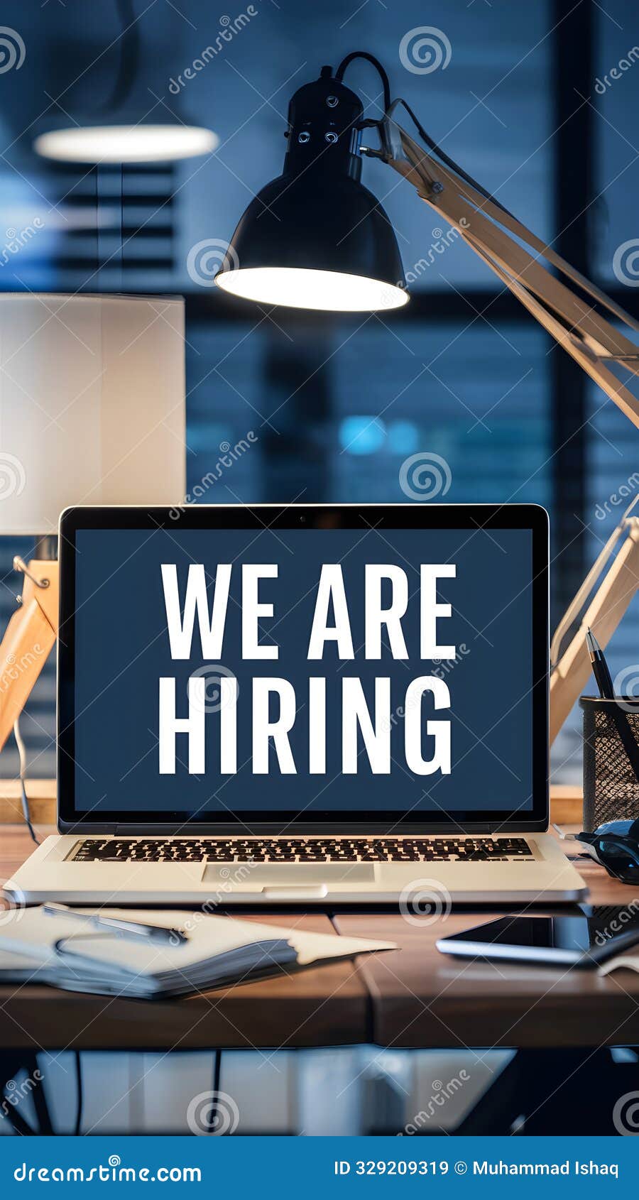 modern office desk, laptop with we are hiring, lamp, pens, blurred backdrop