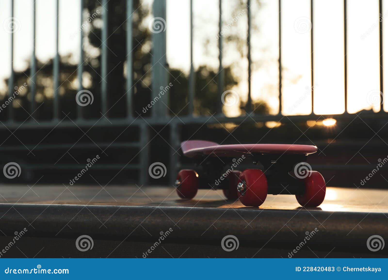 Modern Pink Skateboard with Red Wheels on Top of Ramp Outdoors. Space