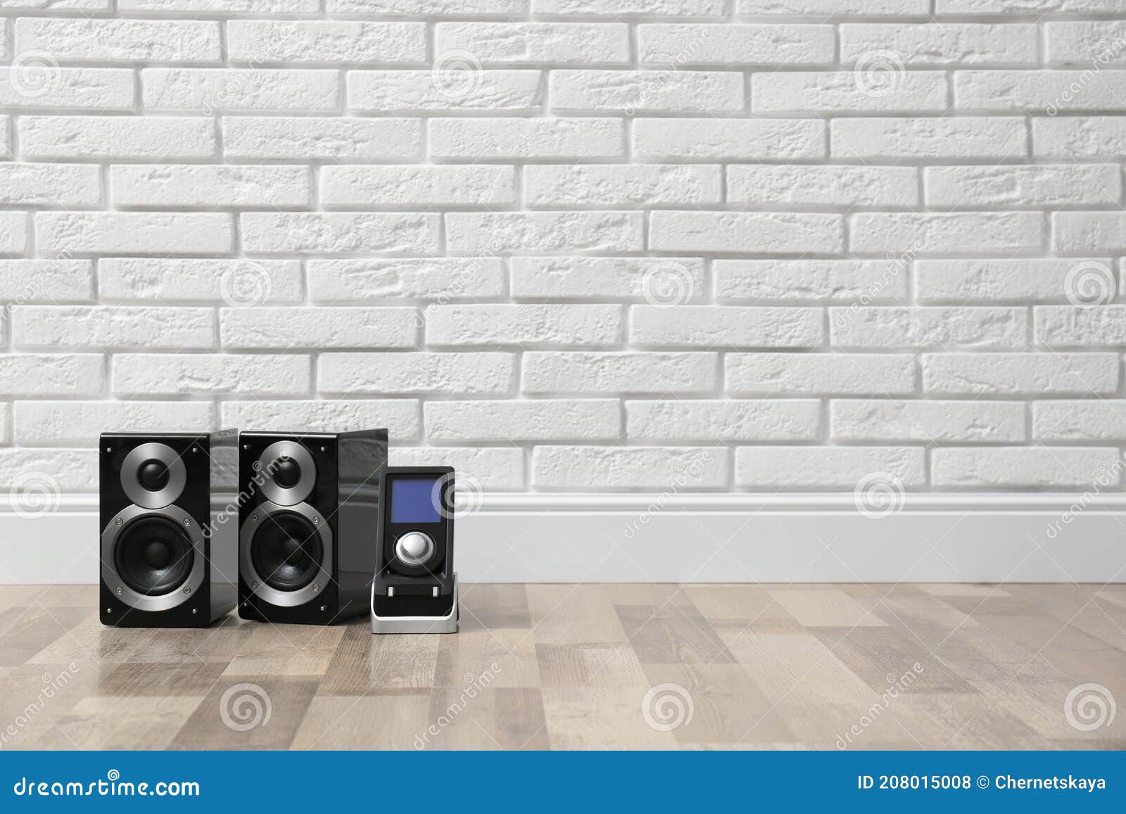 Modern Powerful Audio Speakers and Remote on Floor Near White Brick