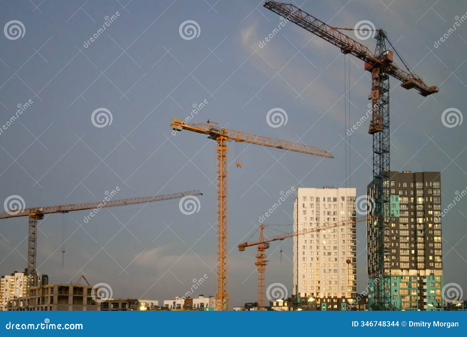 modern tower construction cranes on building site against blue evening sky background
