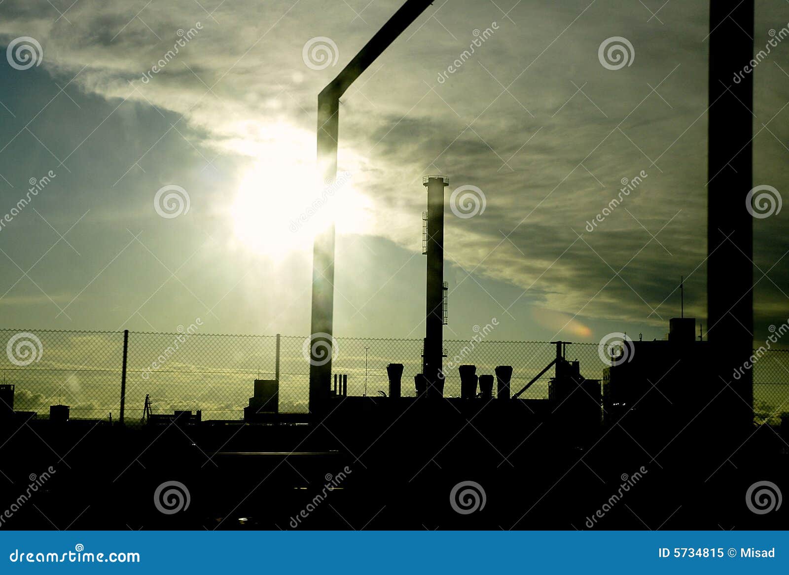 Moderna industriella byggnader silhouetted på skymningen eller gryning med cloudscape och sun som skiner i bakgrund.