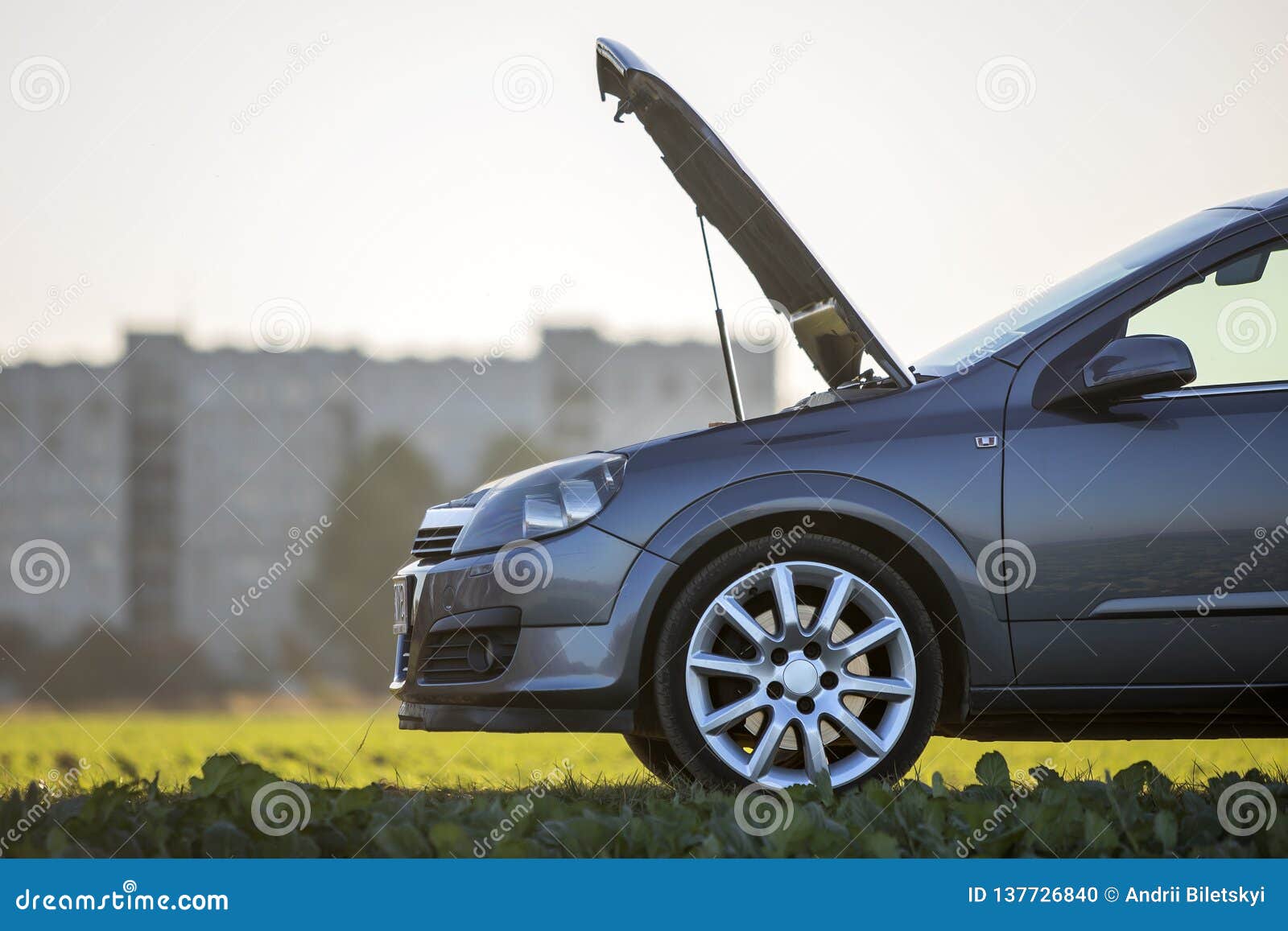 modified image of a fictional non existent car. car with open hood on empty gravel field road on blurred bright sky copy space