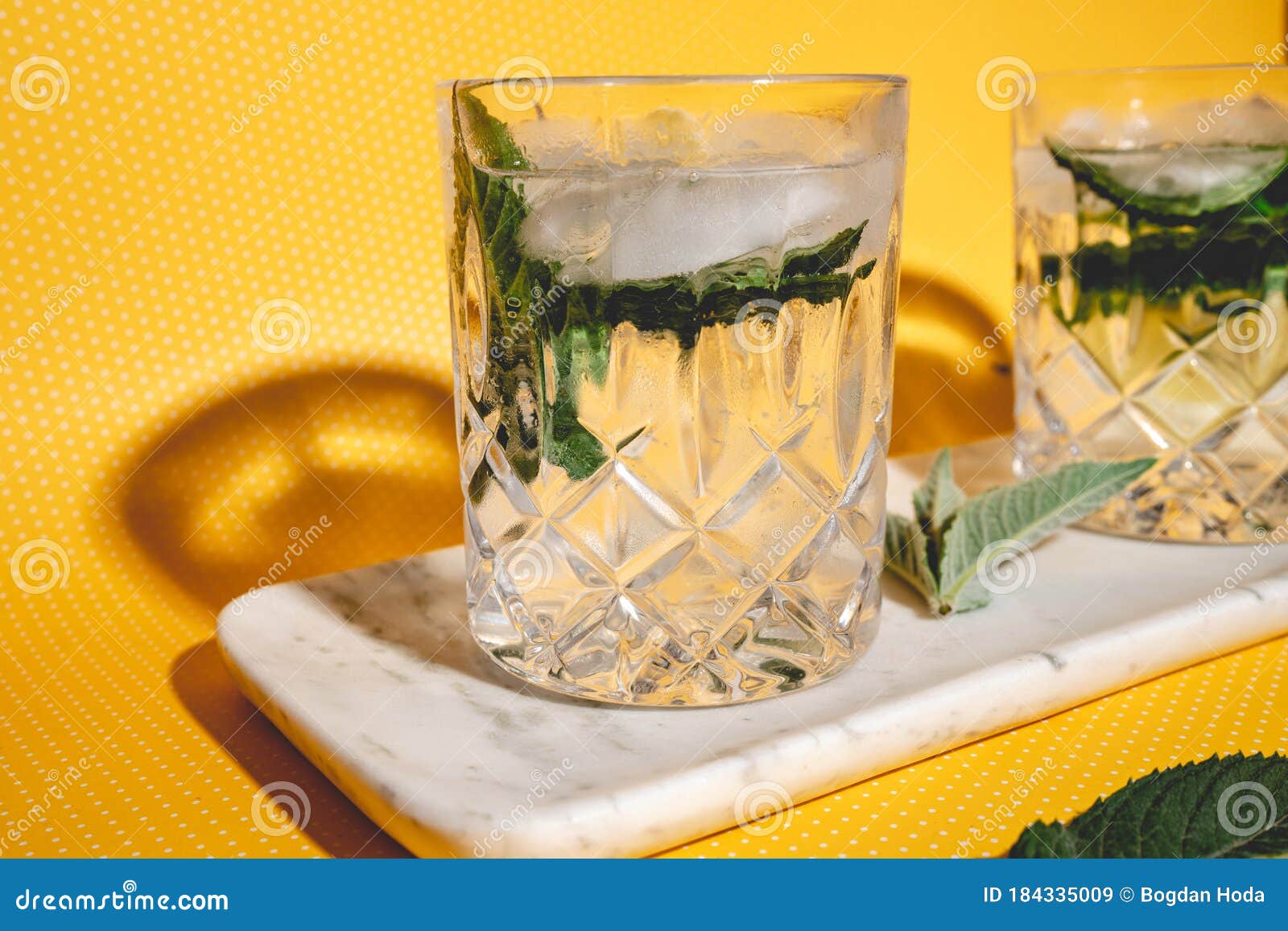 mojito alcoholic cocktails with alcohol, rum lime, mint and ice with hard lights on yellow background. mixology details and close