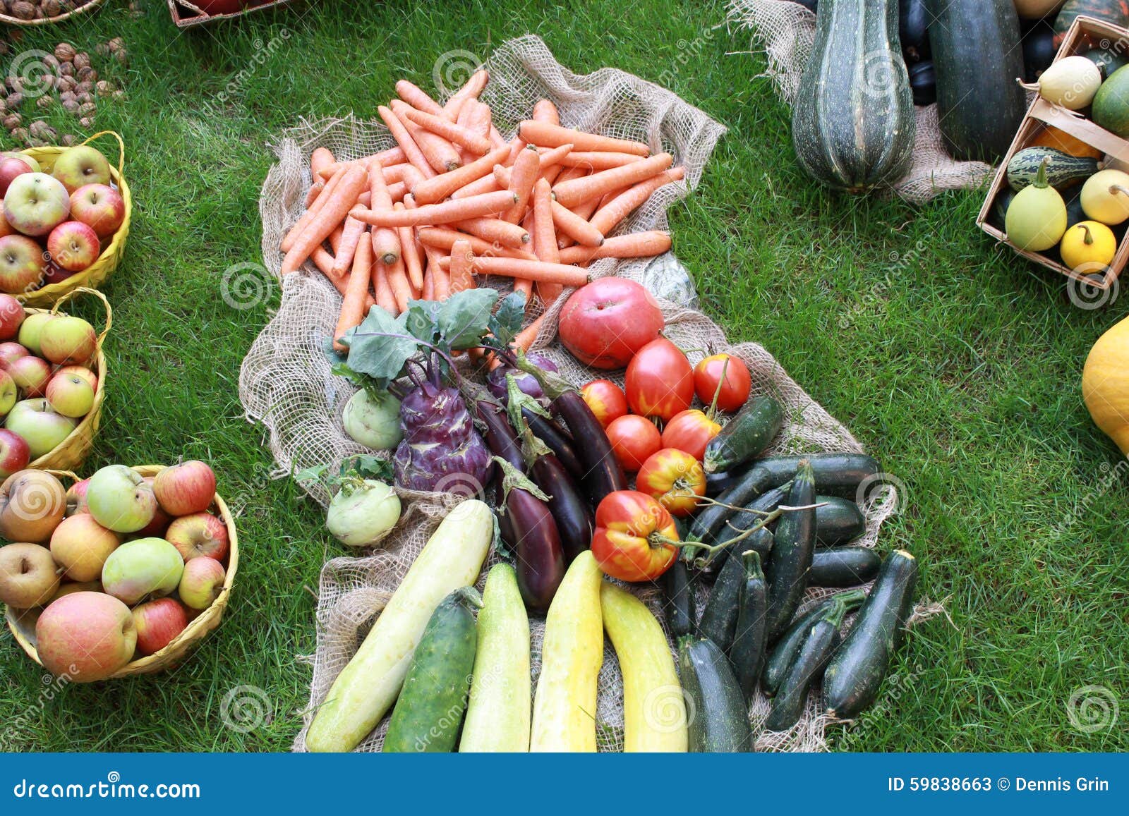 Molte verdure sane differenti in giardino su erba. Un giardino con una palla del fieno con le verdure impilate compreso: Zucche, insalata, mele, carote, cetrioli e molto
