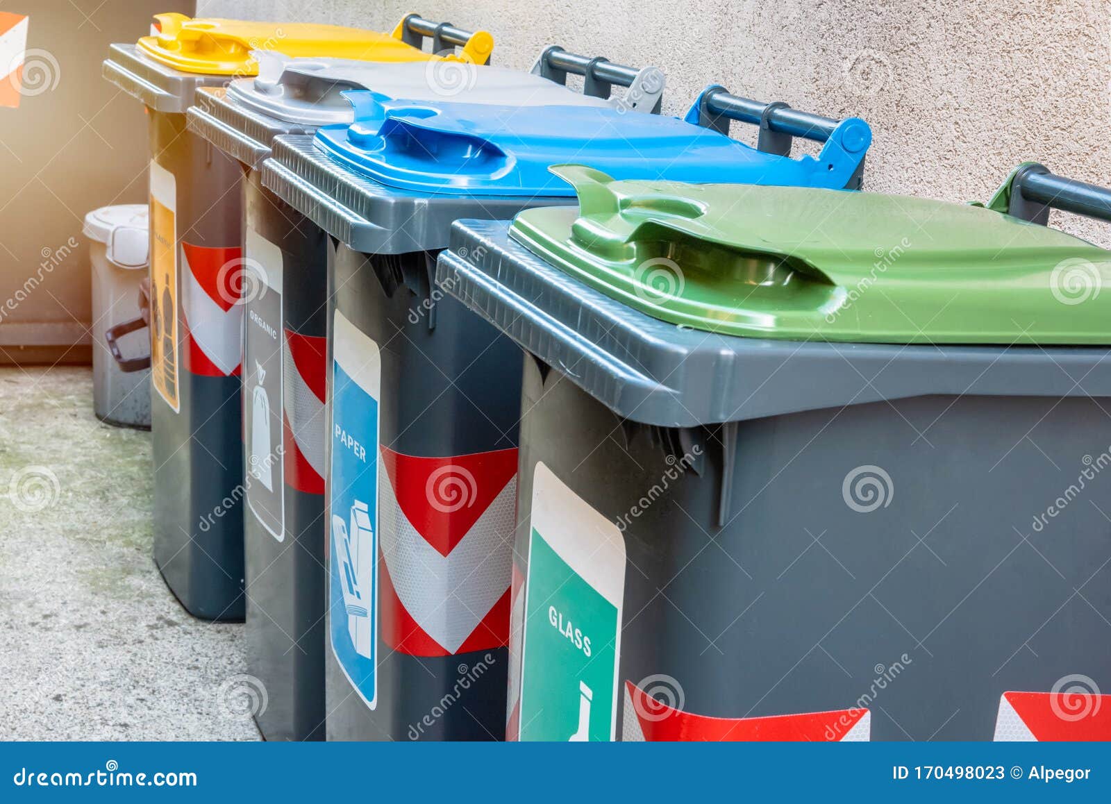 Monete di riciclo lungo la parete esterna di una casa. Fila di bidoni da riciclaggio con coperchi colorati lungo il cortile di una casa Concetto di ecologia