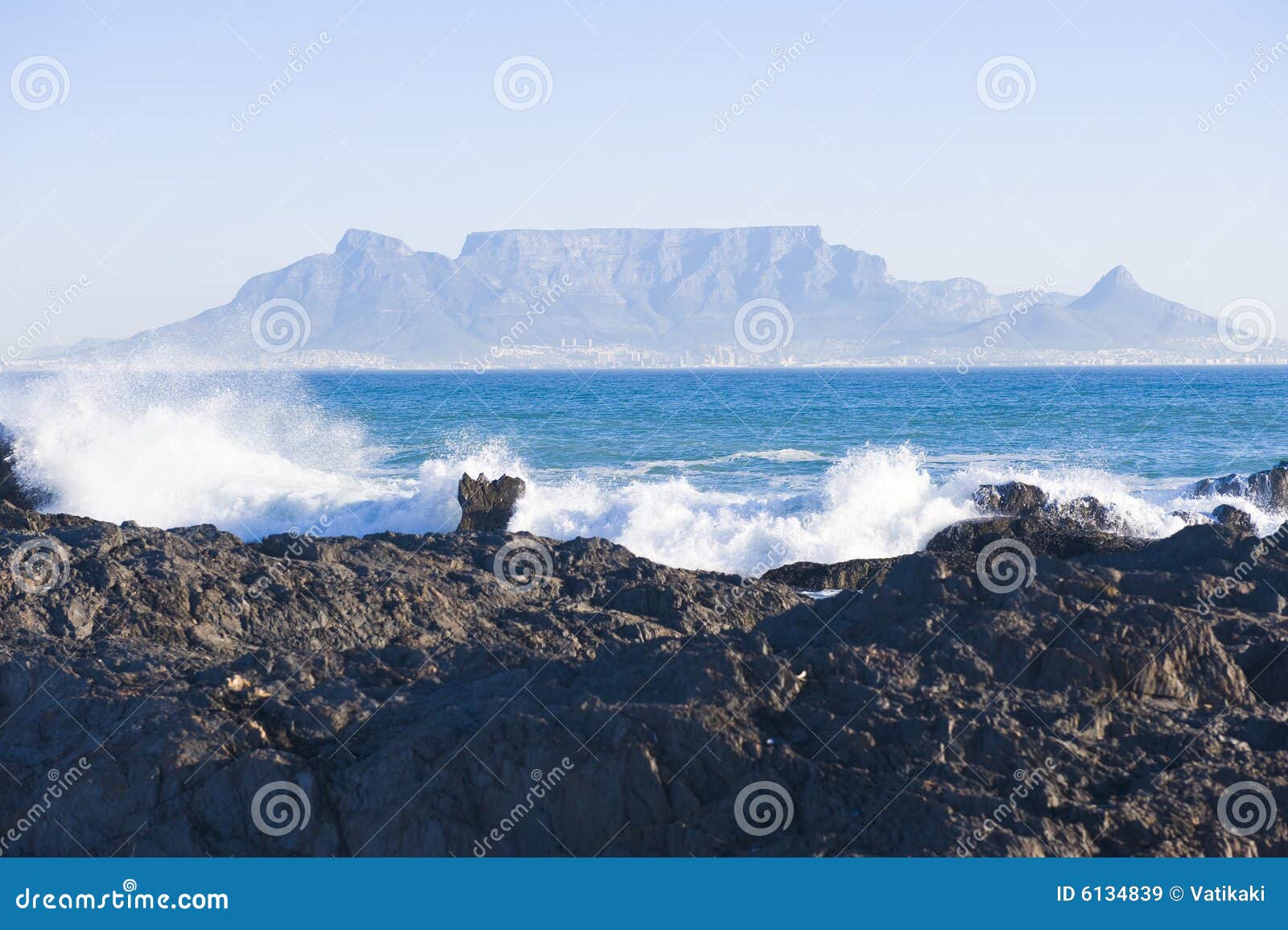 Montanha Cape Town da tabela. Montanha da tabela - o marco mundialmente famoso em Cape Town, África do Sul. Retrate tomado em um dia de invernos desobstruído da praia da costa de Blouberg. Uma parte rochosa da praia está no primeiro plano.