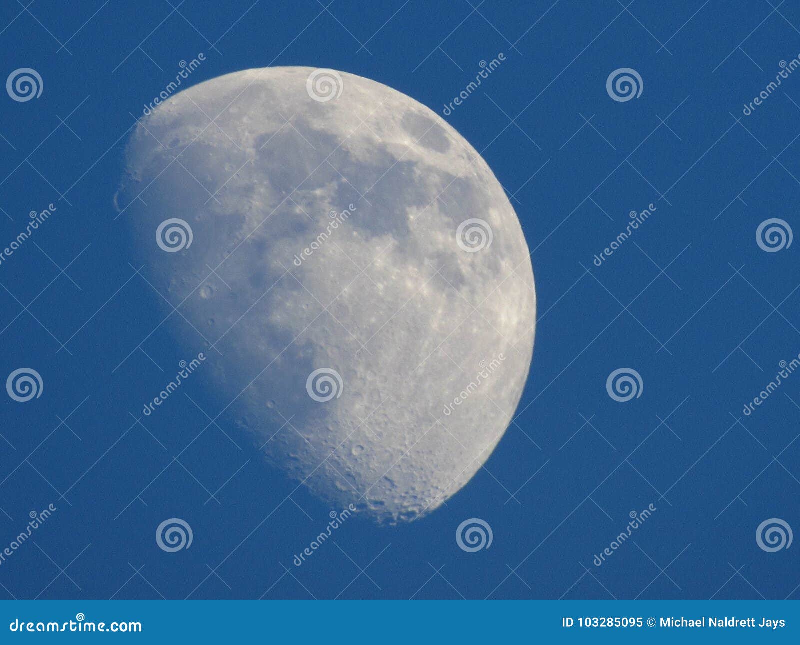 Moon at Dusk. Deep blue sky surrounding a well illuminated moon fading into the background. Displays a reasonable amount of the lunar surface including craters and dark spots