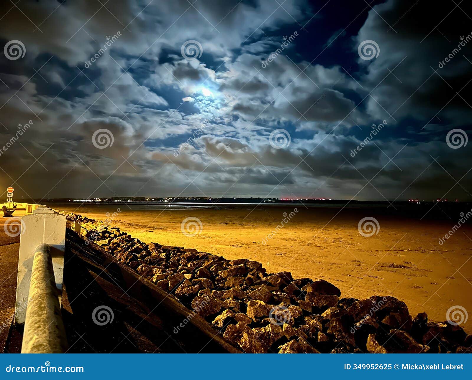moonlit night over the bay of somme from le crotoy, illuminating dramatic clouds, golden sand, and coastal rocks with village