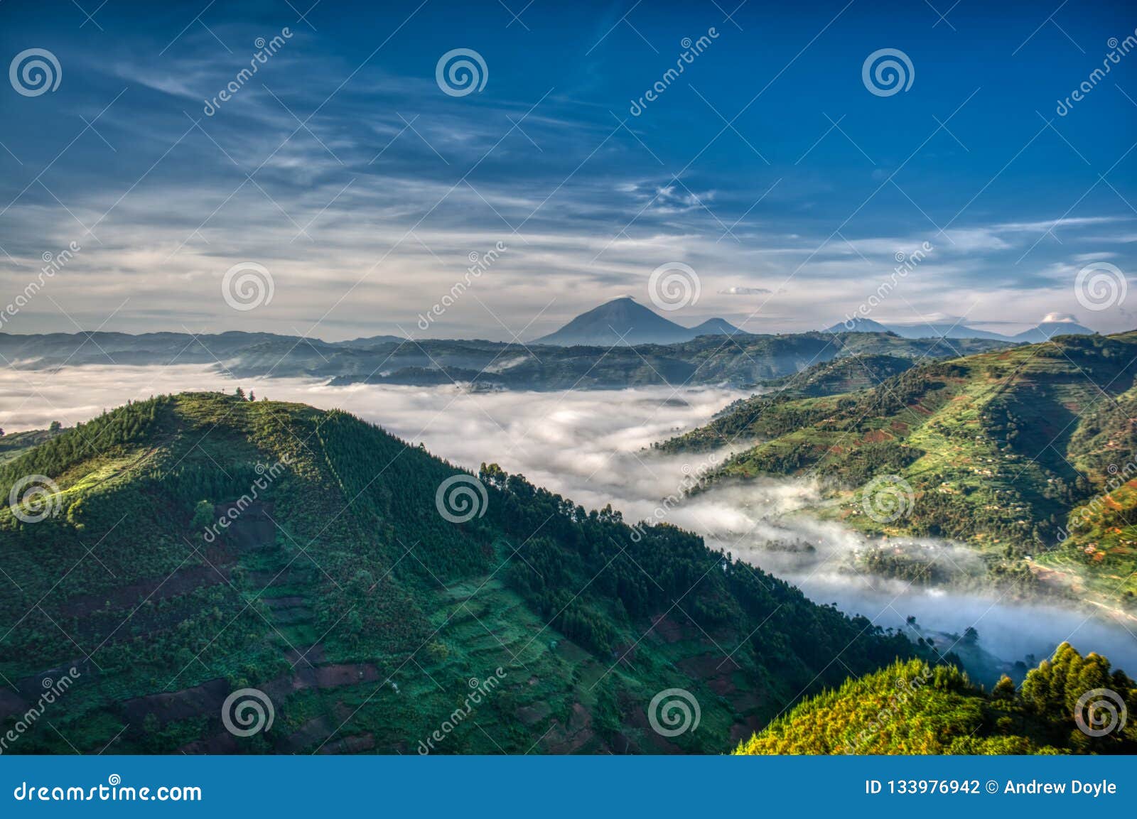 morning in uganda with volcanoes in background, fog in the valley and farmlands stretching far
