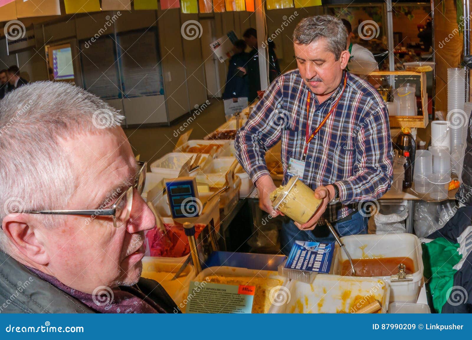 Moscú, Rusia - 25 de febrero de 2017: El vendedor canoso del hombre en la feria llena un tarro de la miel producida casera para el comprador