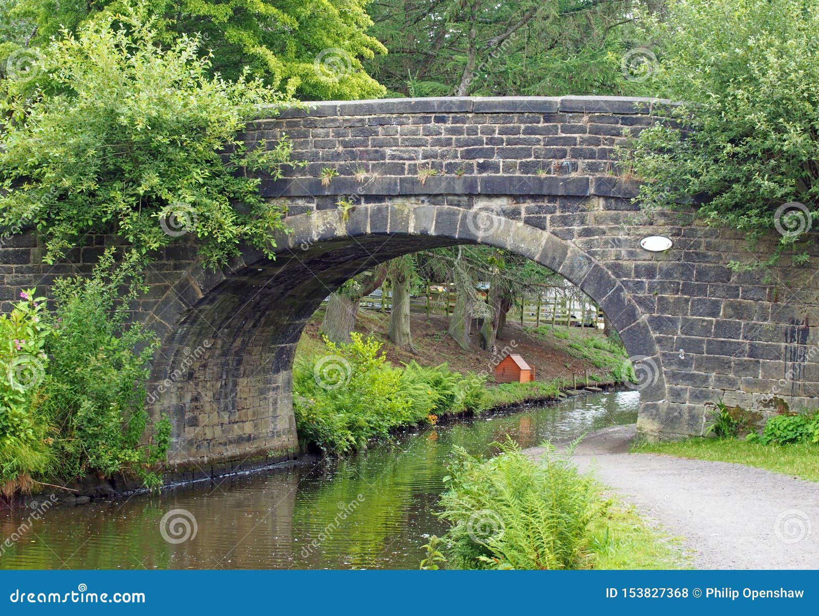 Stary most kamienny przecinający kanał rochdale w hrabstwie Mytholmroyd west Yorkshire z drogą wodną otoczoną drzewami i krzewami