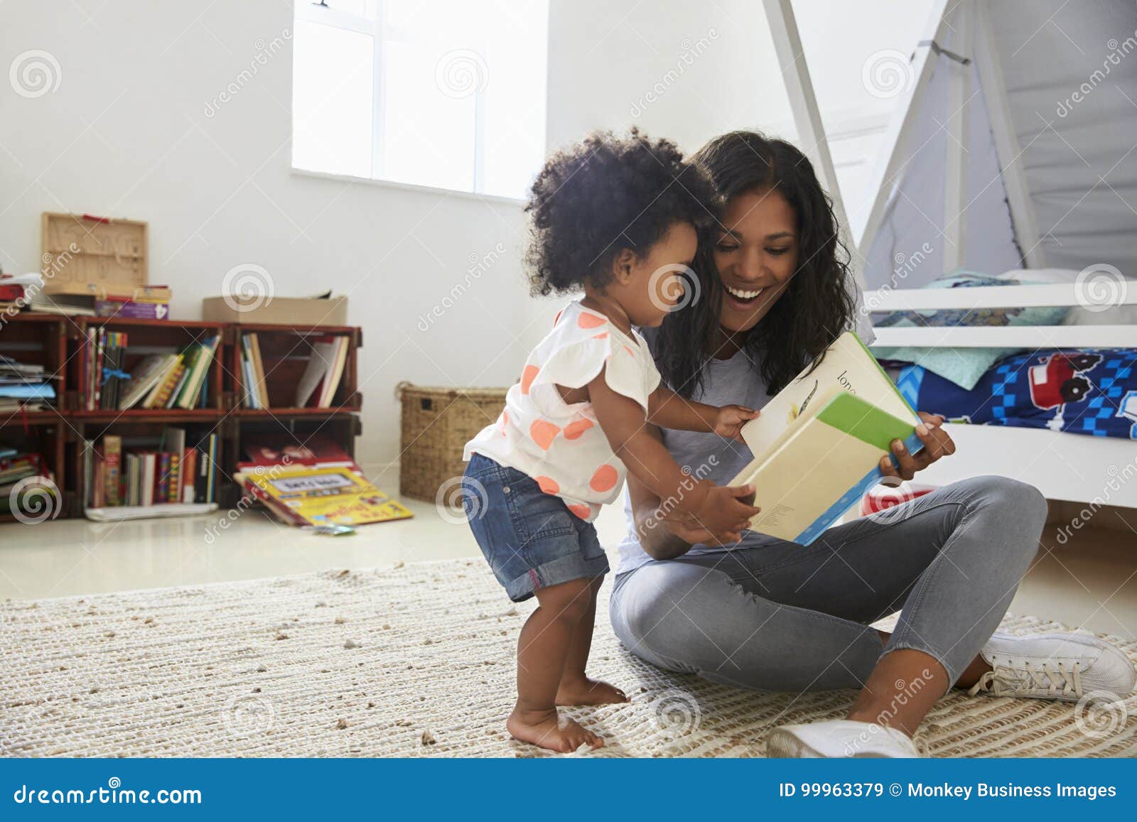 mother and baby daughter reading book in playroom together