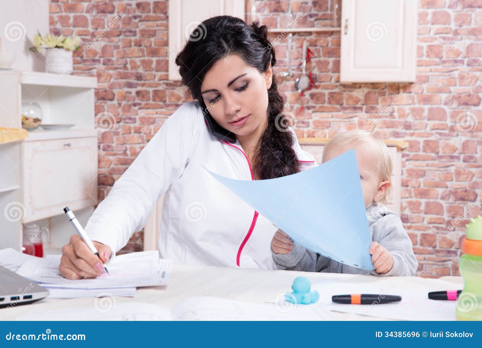 Mother and baby in home office. Mother with baby in the kitchen working with documents and speaks by phone