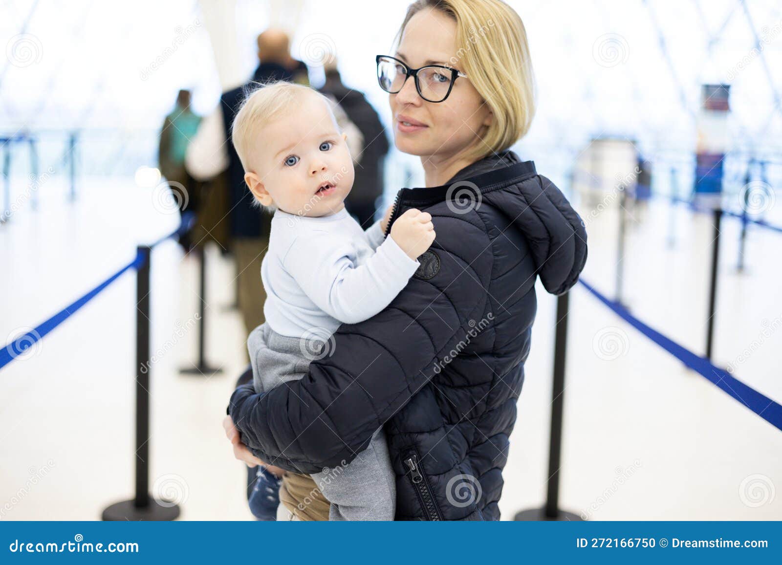 mother carying his infant baby boy child queuing at airport terminal in passport control line at immigrations departure