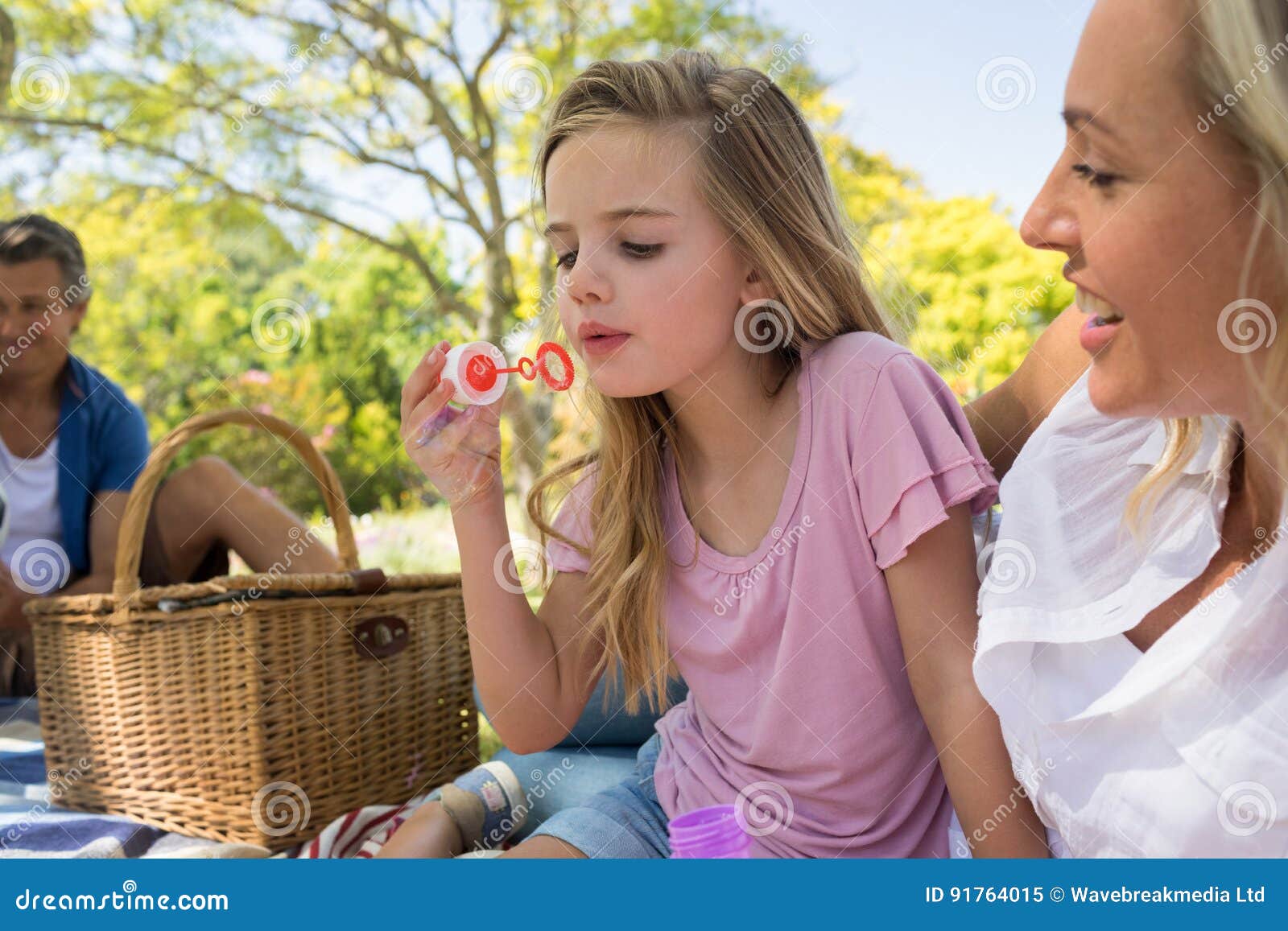 Mother And Daughter Blowing Bubble With Bubble Wand At Picnic In Park