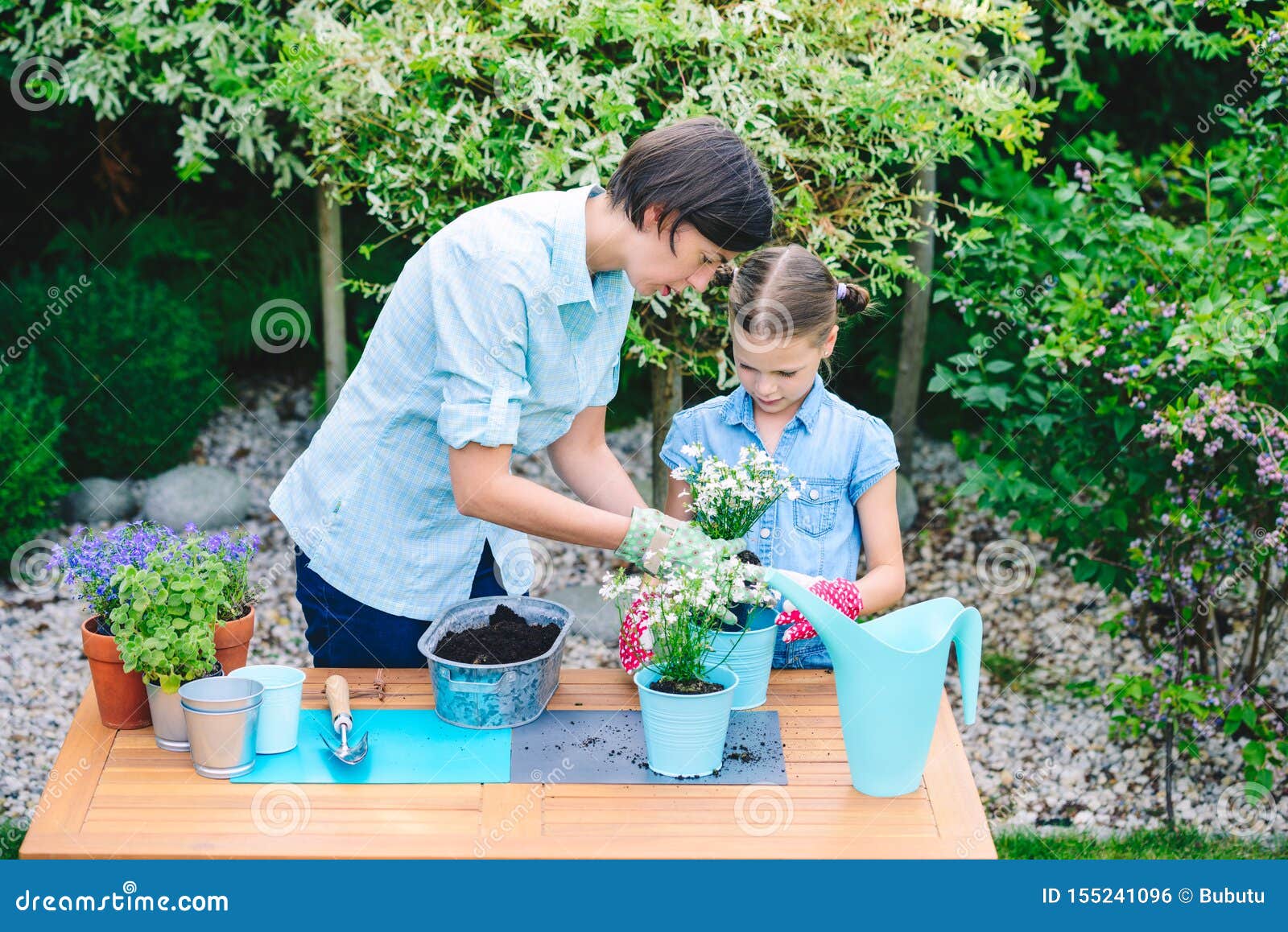 mother and daughter planting flowers in pots in the garden - concept of working together, closeness