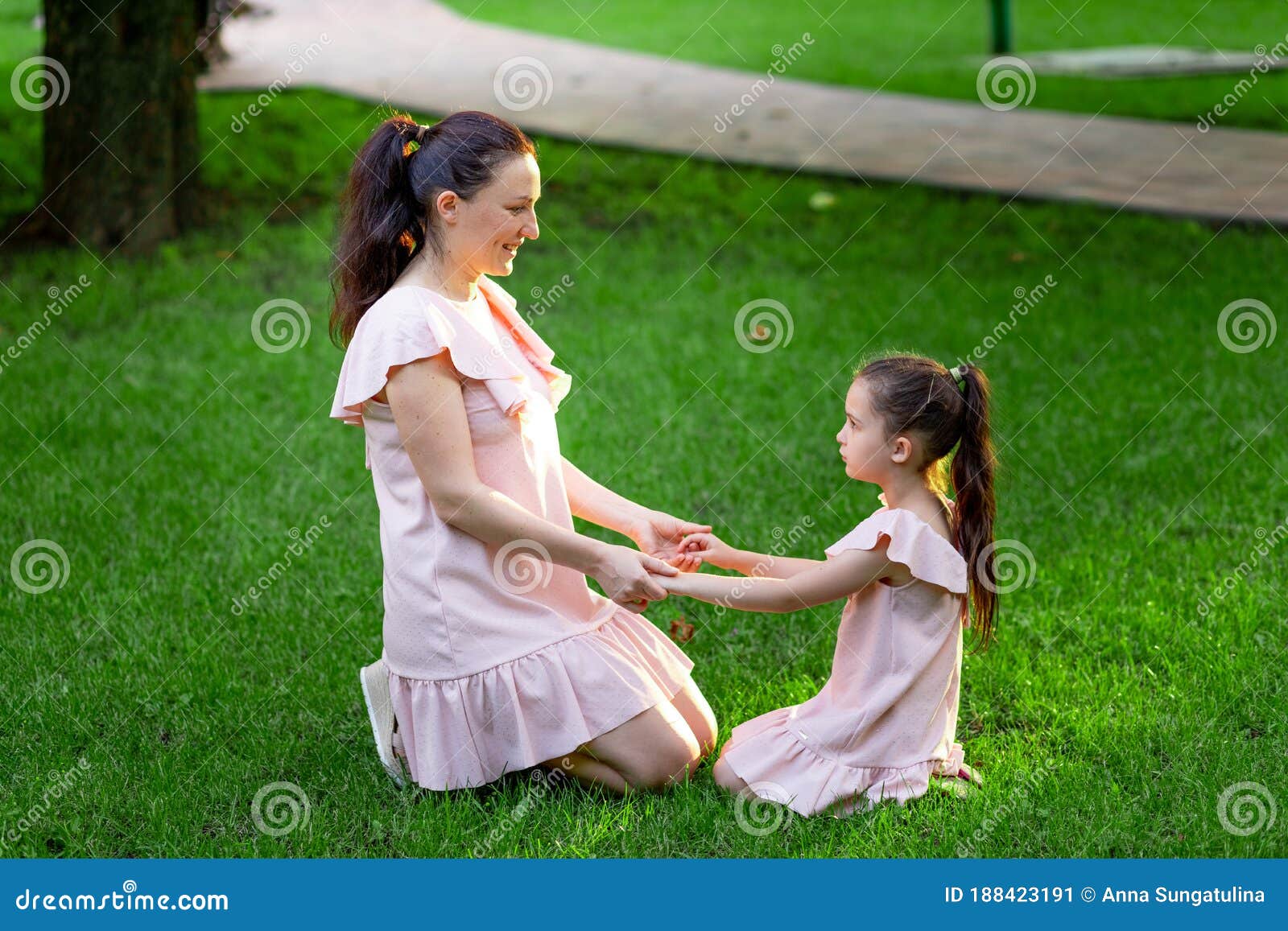 Mother And Daughter 5 6 Years Old Sit In The Park On The Grass And Hold Hands In The Summer A 