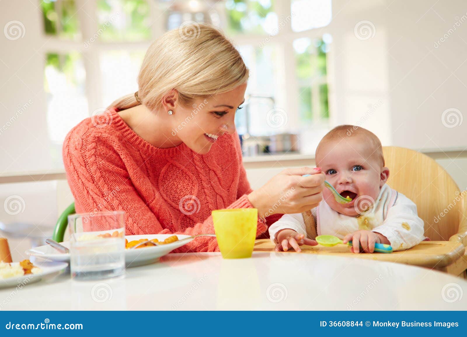 mother feeding baby sitting in high chair at mealtime