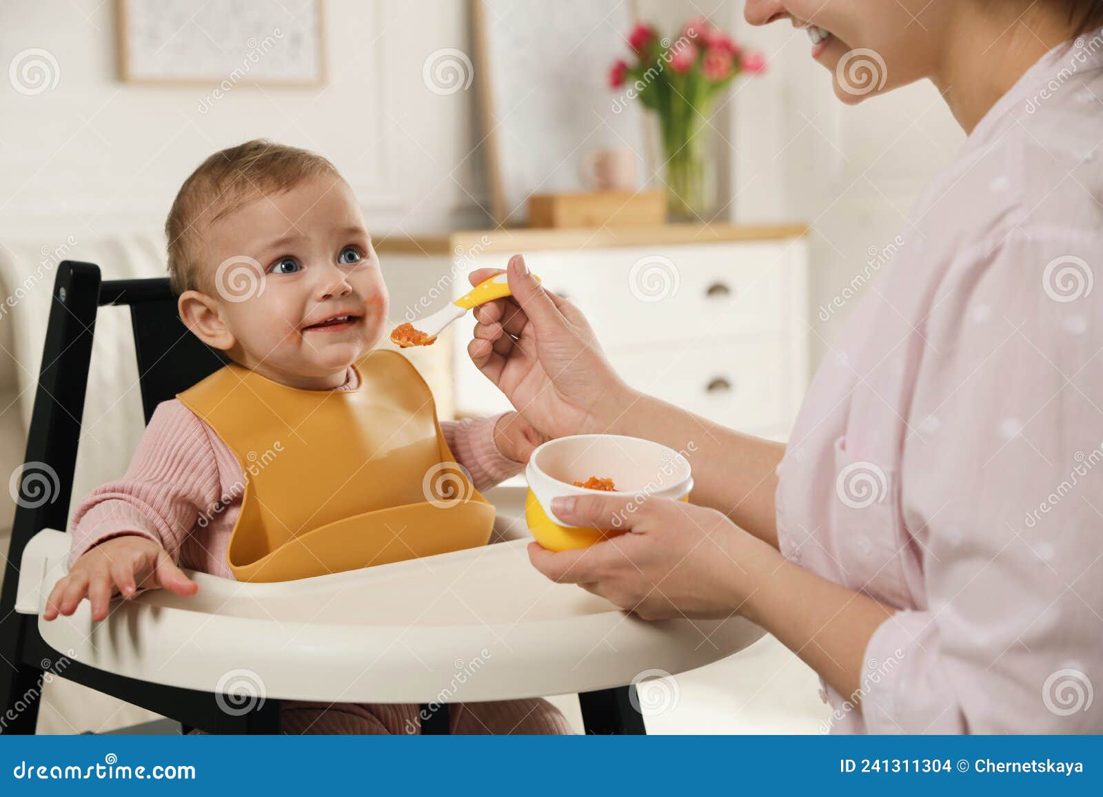 mother feeding her little baby at home. kid wearing silicone bib