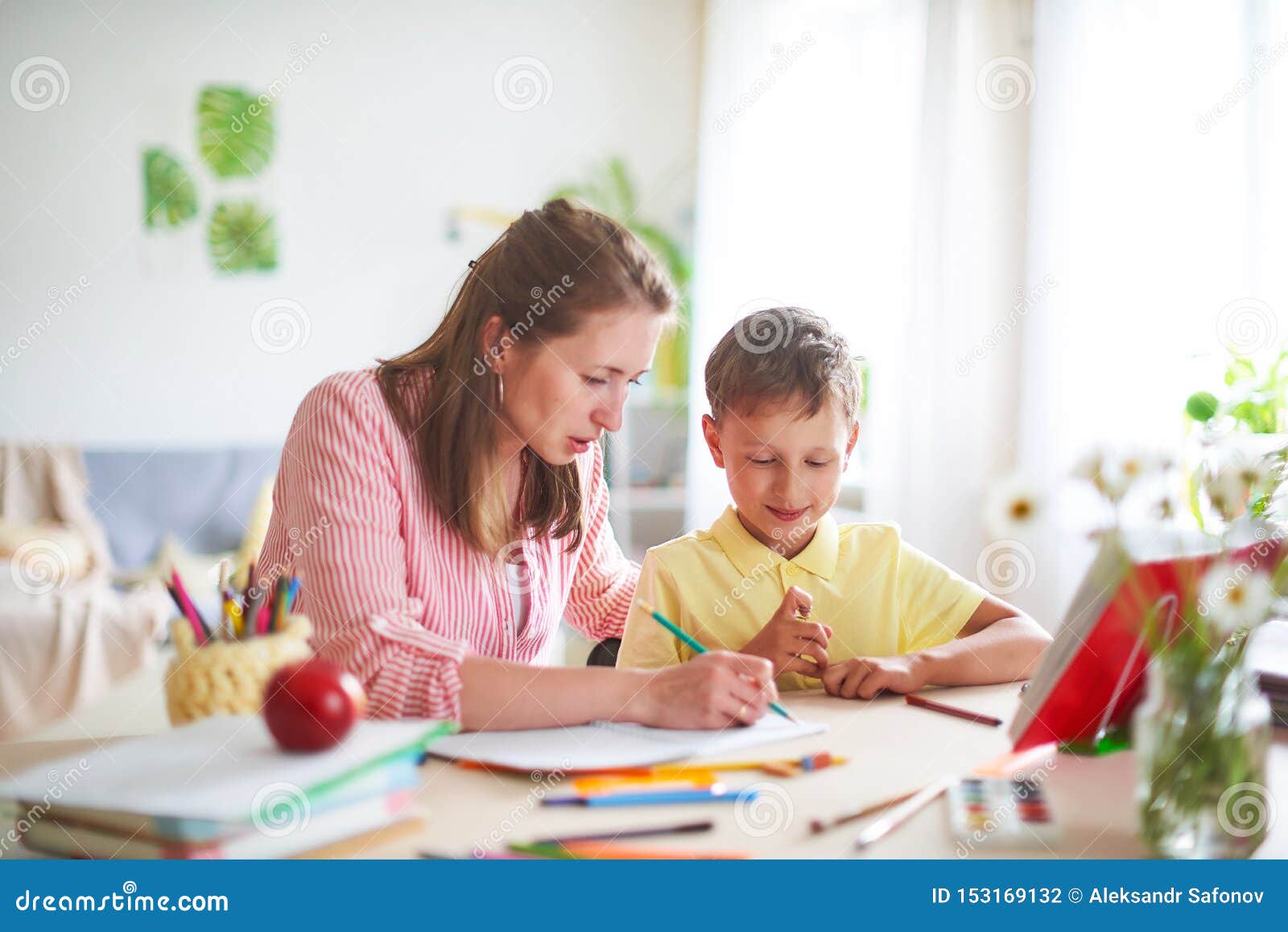 mother helps son to do lessons. home schooling, home lessons. the tutor is engaged with the child, teaches to write and count