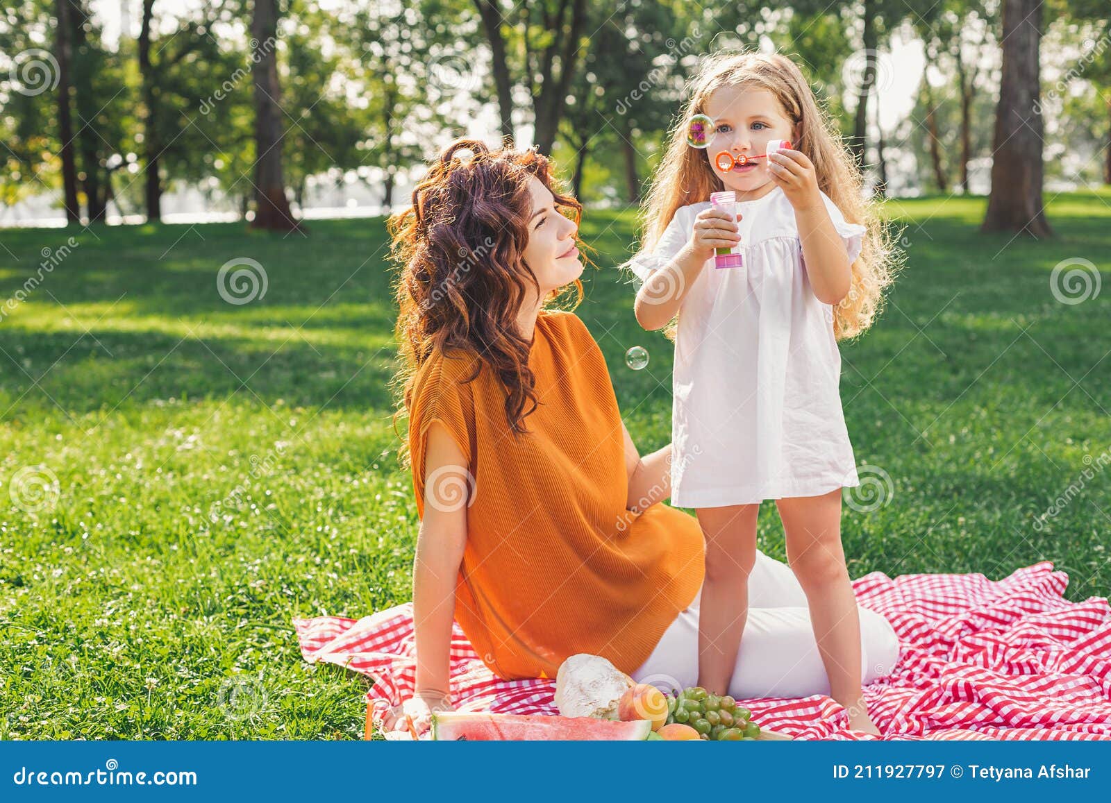 mother looking her daughter blowing sopa bubbles in the park