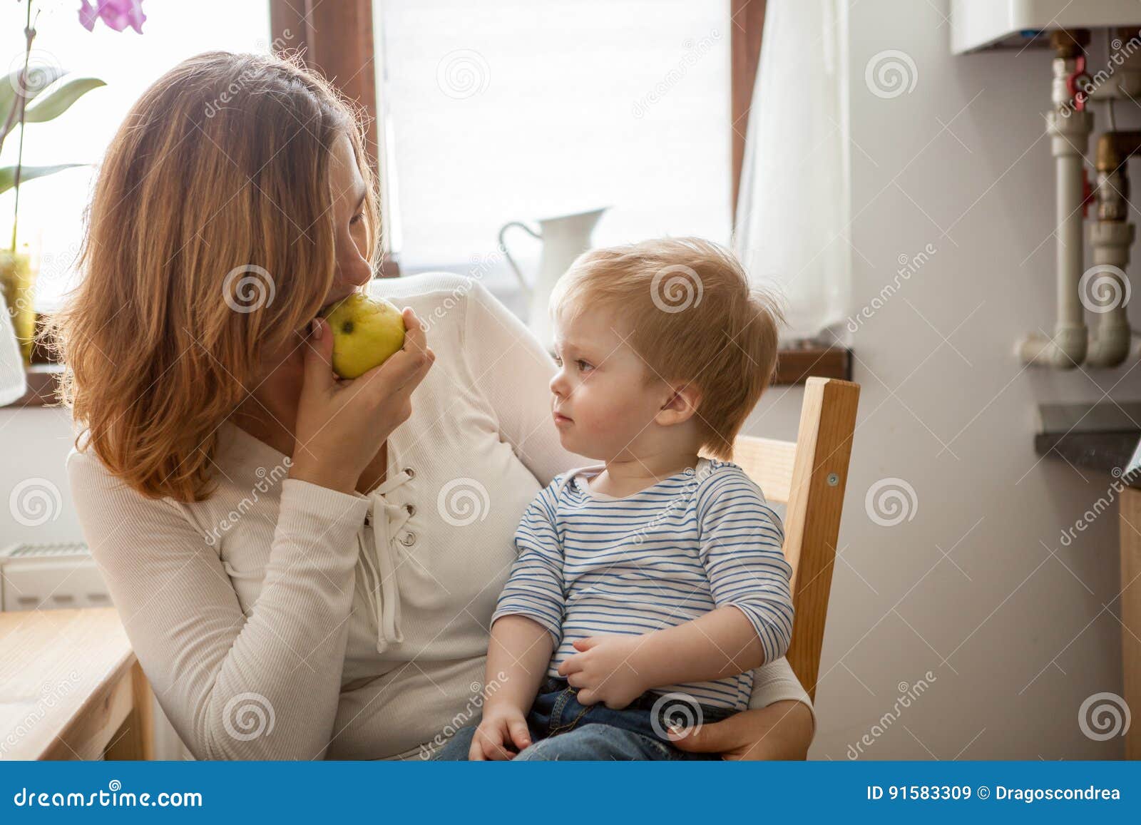 Mother and son eating an apple at the kitchen. Happy childhood and parenting