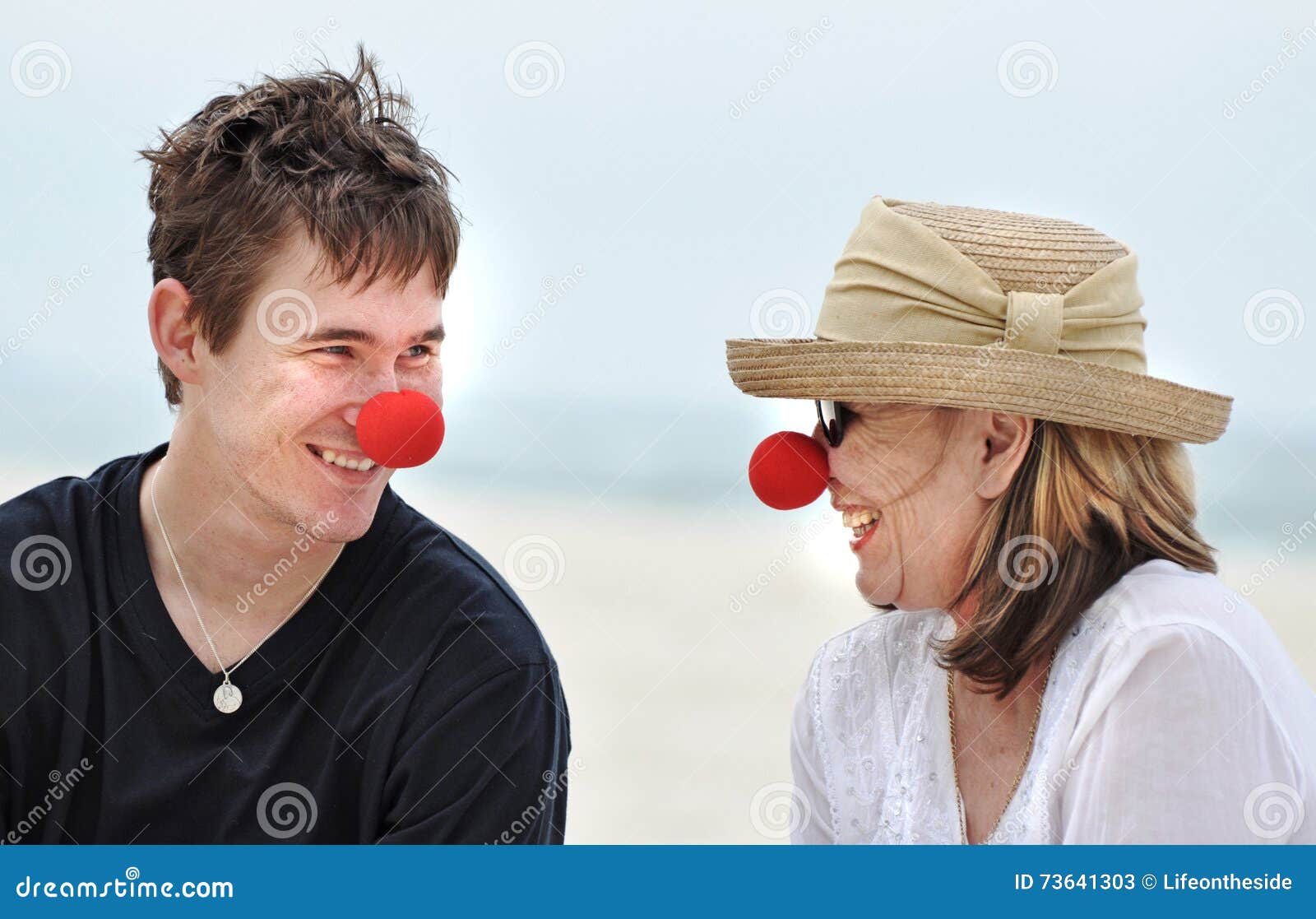 mother and son having fun laughing celebrating red nose day on beautiful beach holiday