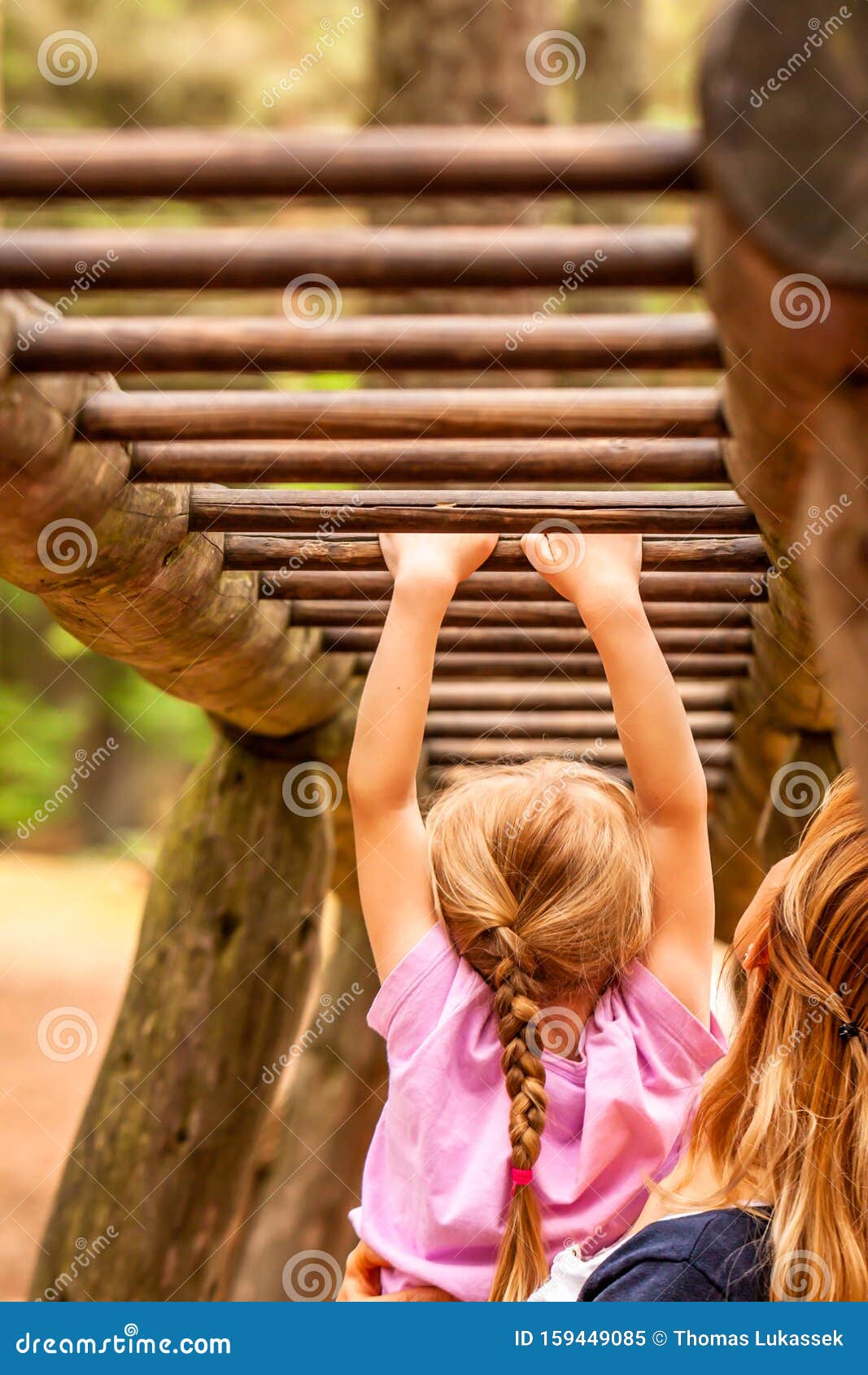 mother supporting daughter in the playground with climbing and hanging on a ladder