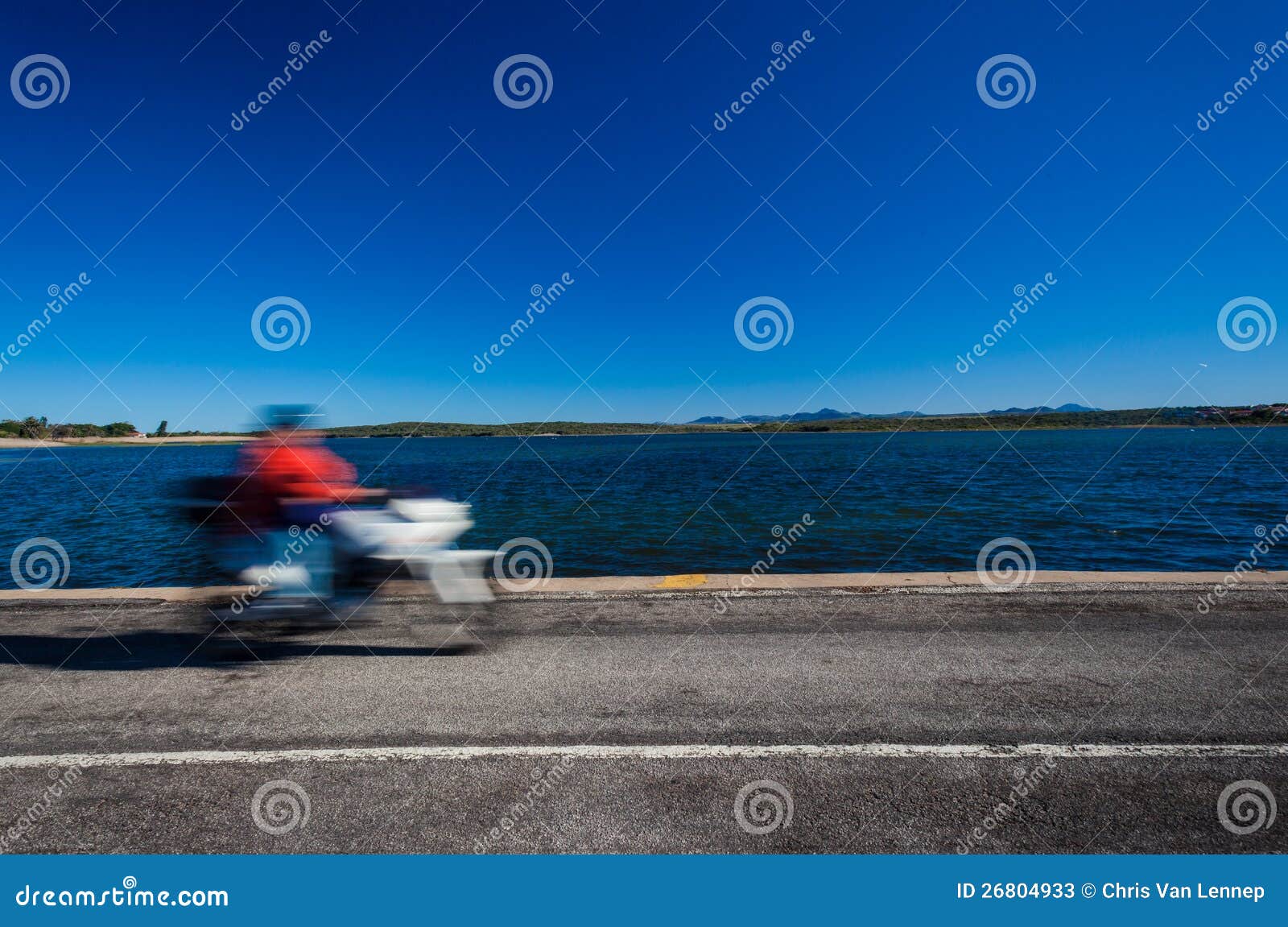 Motocyklu Prędkości Plamy Błękitny Laguny Droga. Barwi fotografii wizerunek niezidentyfikowany motocyklu chodzenie przez horyzontalną ramę w ruchu lub prędkości plamie. szeroki kąta obiektywu obrazek na niskiego pozioma droga na grobli nad rzeczną laguną z asfaltowej drogi szczegółem i niezidentyfikowaną jeźdza niezidentyfikowany - przodu i błękitny szeroką rzeczną laguną odległy krajobraz w przedpolu.