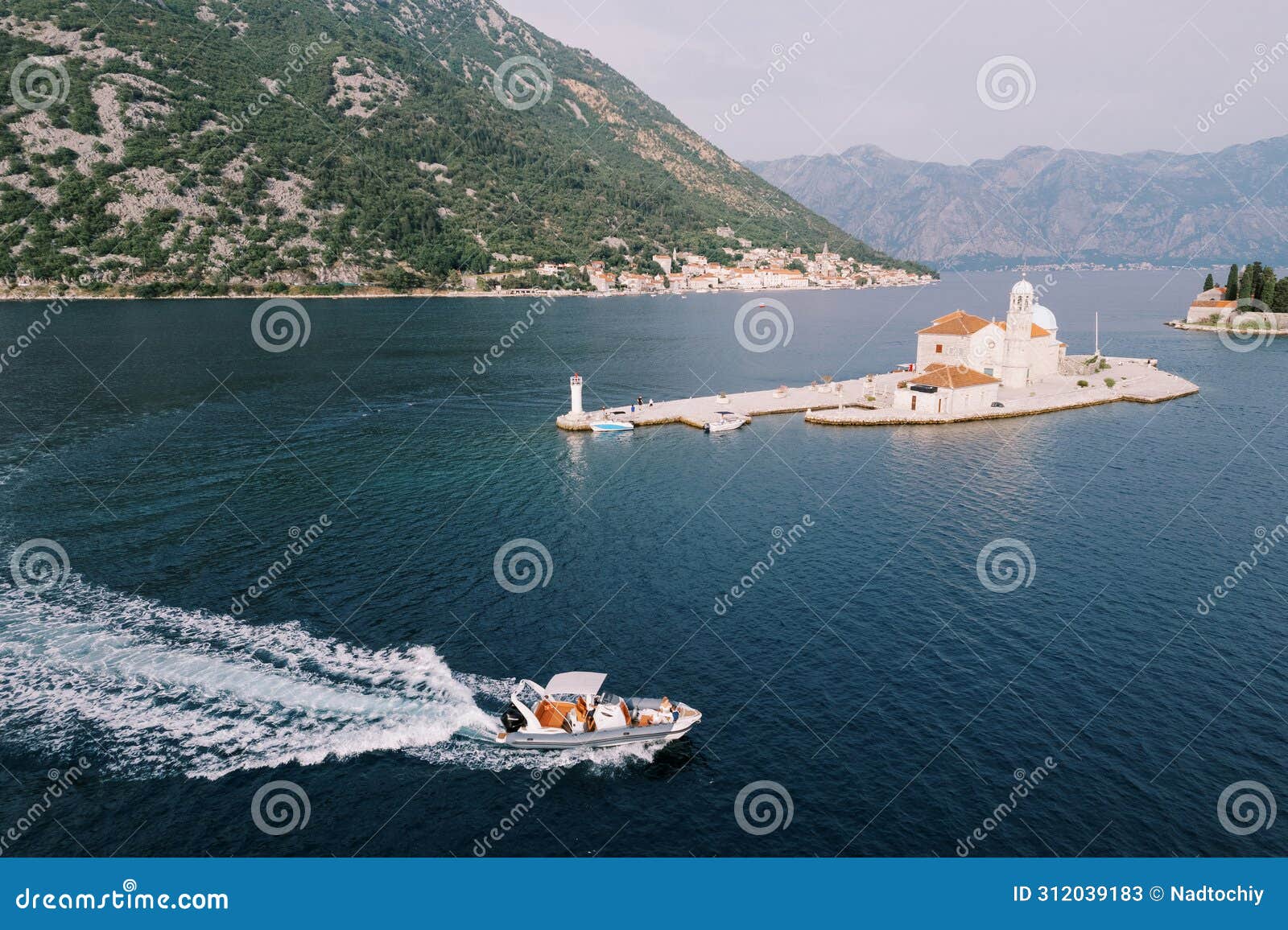 motorboat sails on the sea past the church of our lady on the rocks of the island of gospa od skrpjela. montenegro