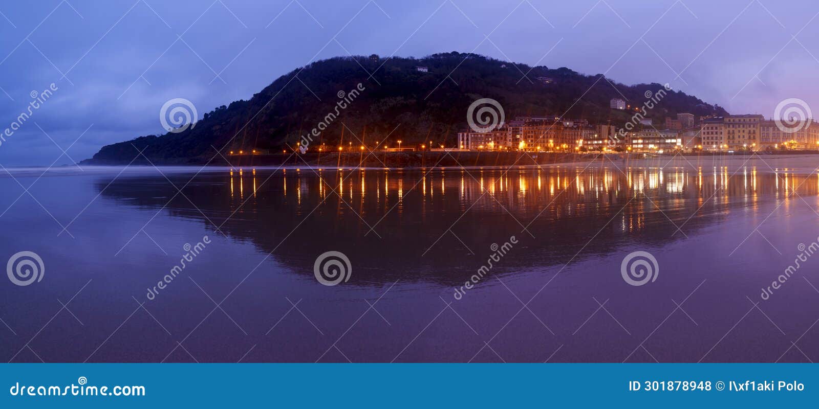 mount uliÂ­a and zurriola beach. mount ulia and the lights of the city reflected in the zurriola beach at sunrise.