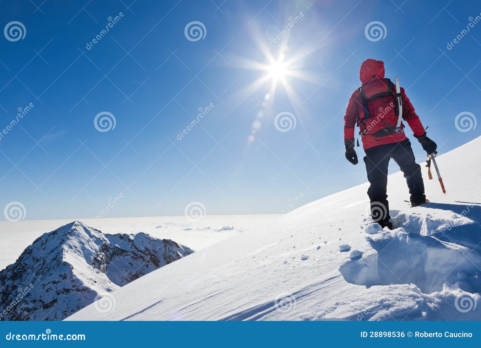 mountaineer reaches the top of a snowy mountain in a sunny winter day.