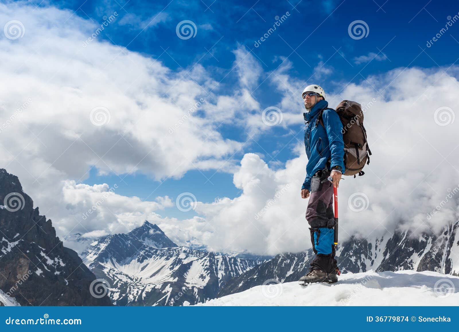 mountaineer reaches the top of a snowy mountain in a sunny winter day