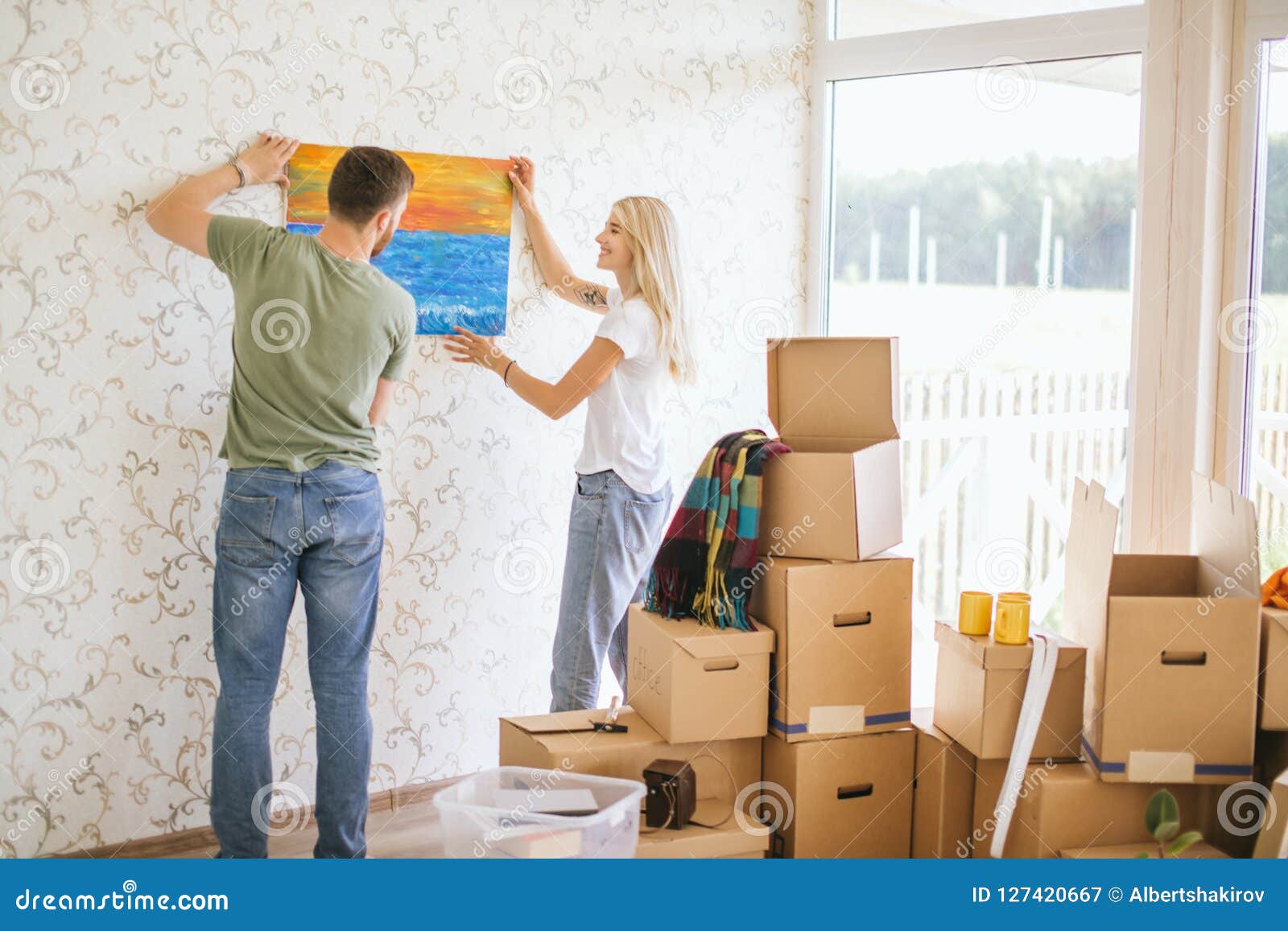 Moving House Couple Hanging Picture On Wall In New Home