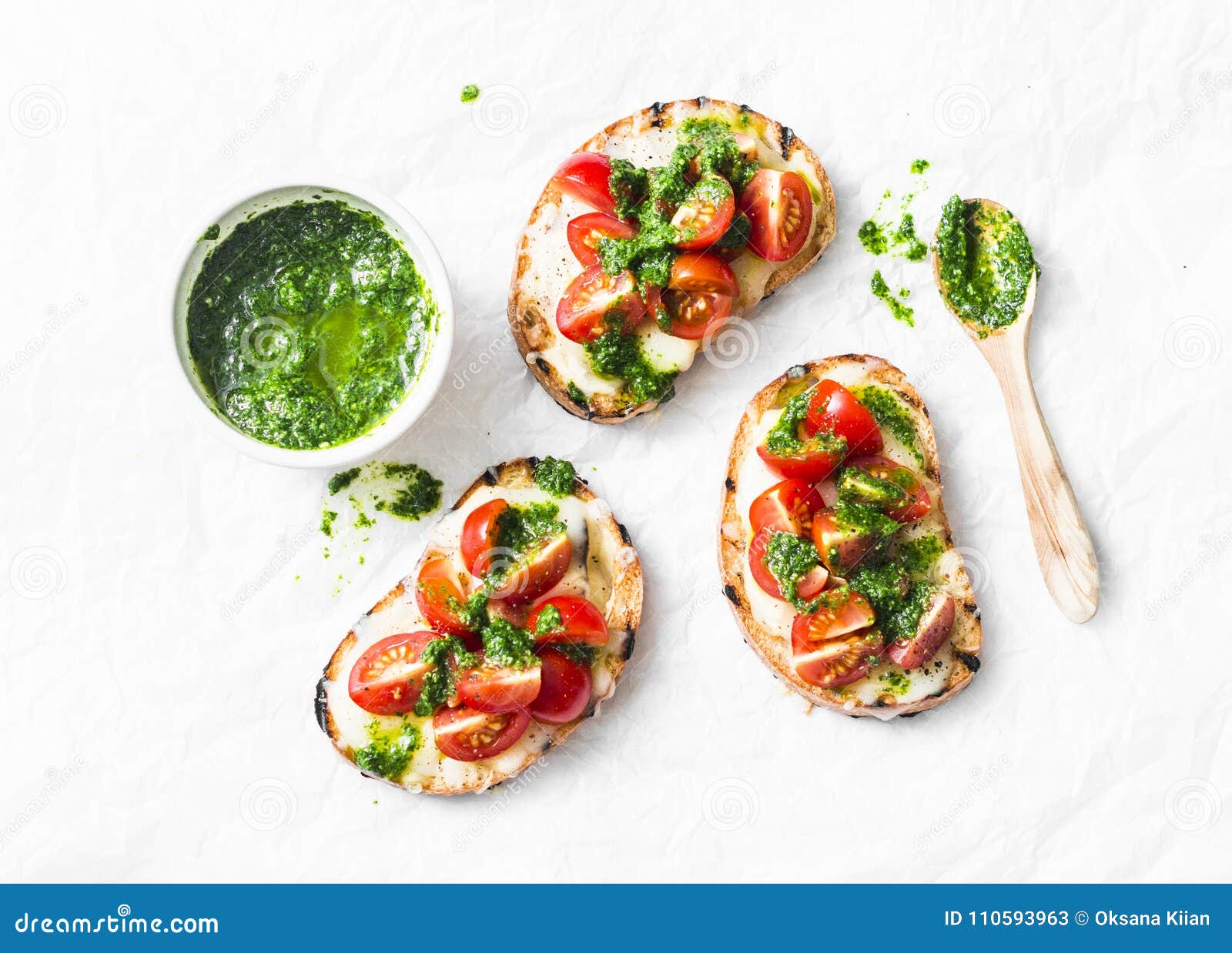 mozzarella cheese, cherry tomatoes and arugula pesto bruschetta on light background, top view. arugula pesto and sandwiches - tast