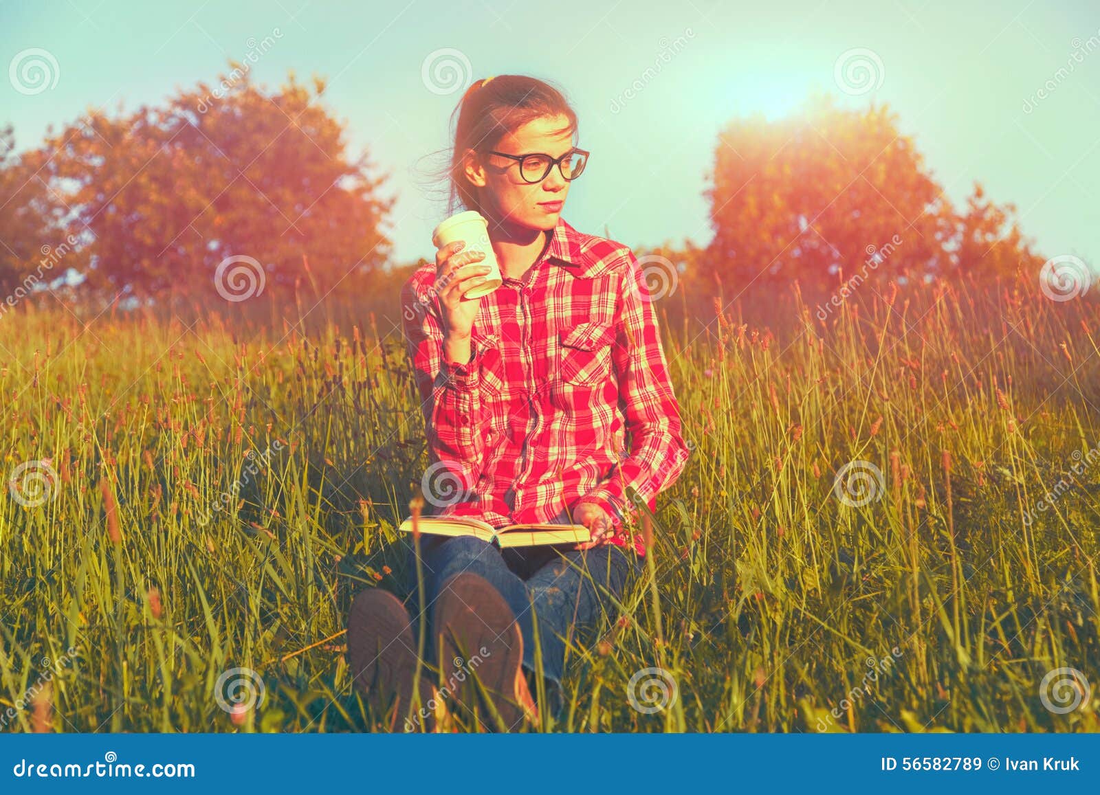 Muchacha con la taza y el libro de café que goza en hierba del verano